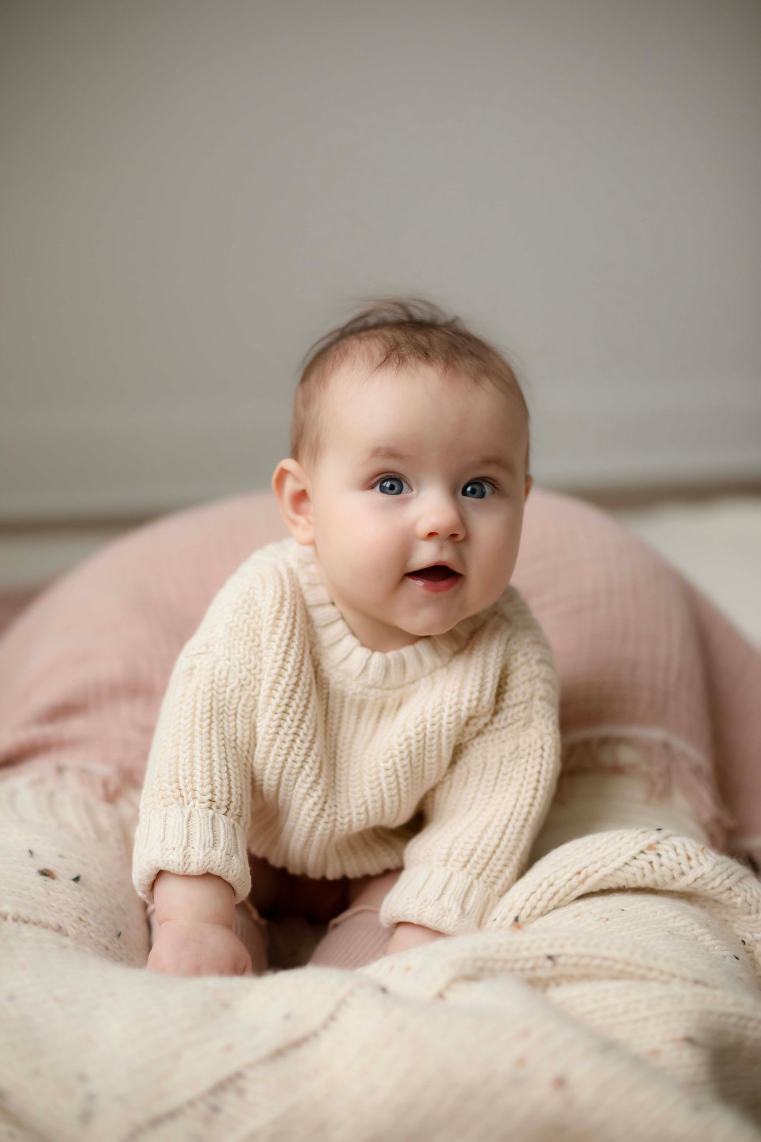 Baby in cream knit sweater lying on soft pink bedding in a series of sweet candid poses.