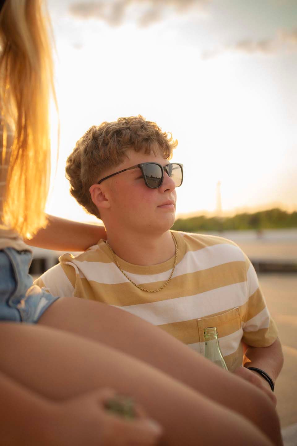 Young man in striped shirt and sunglasses relaxing outdoors during golden hour sunset.