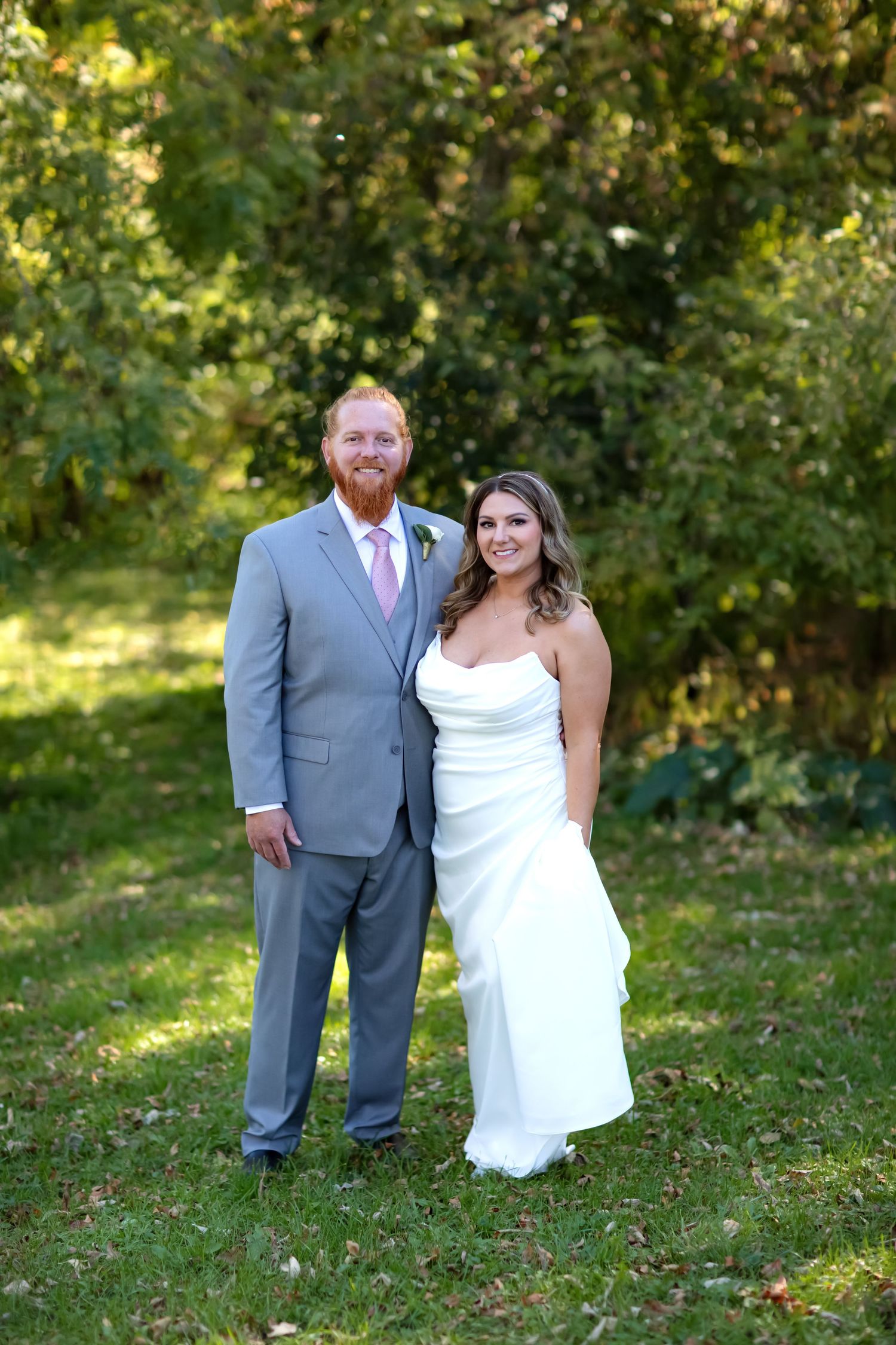 A wedding couple poses together outdoors in a garden setting with natural greenery in the background.