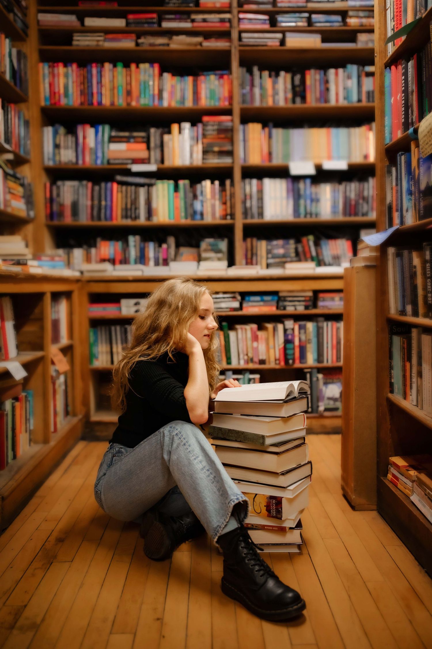 A contemplative moment among library stacks with books piled on wooden floors.
