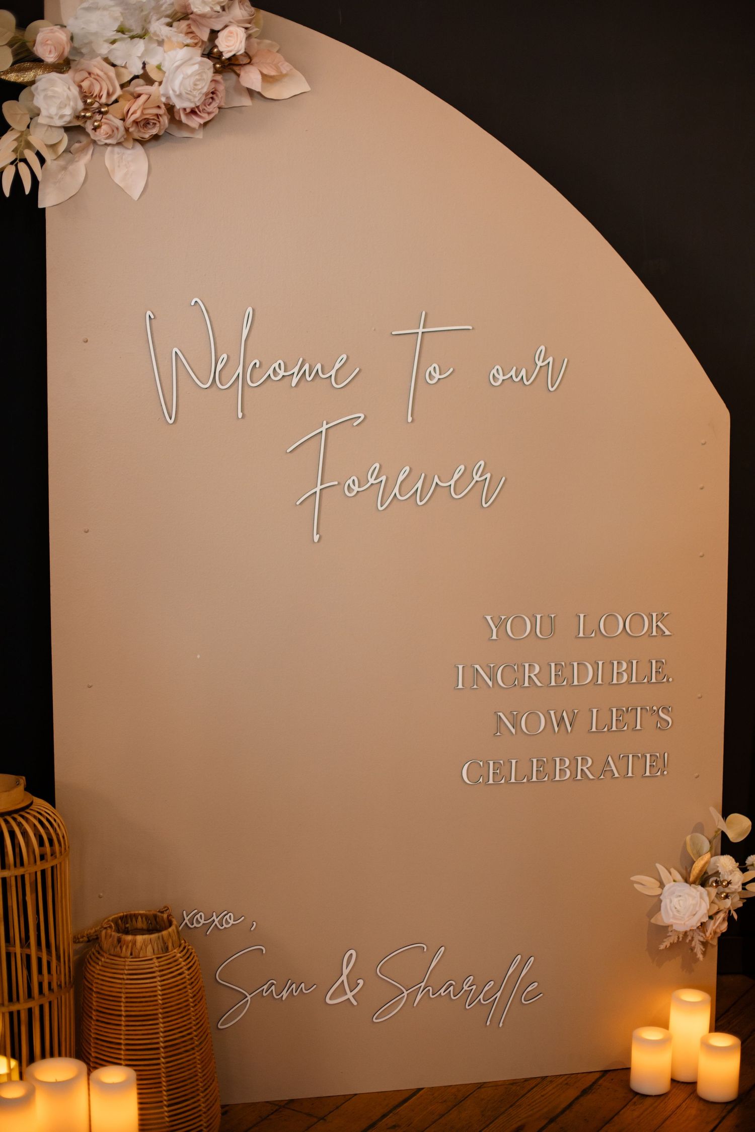 Elegant wedding welcome sign with white neon text and floral decorations against a beige curved backdrop.