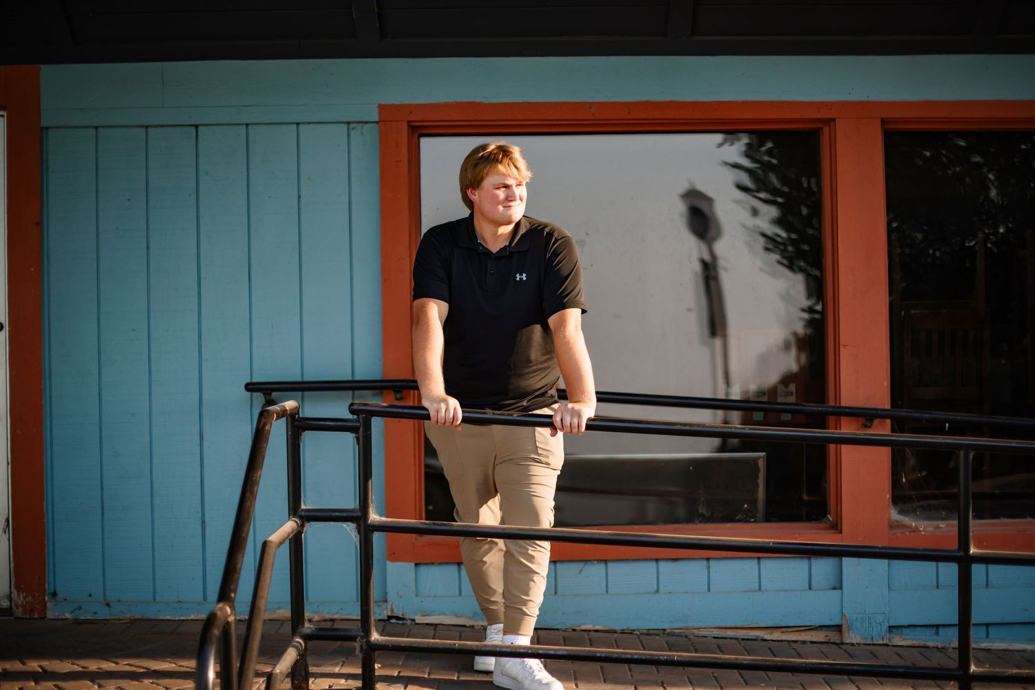 Baseball player in casual attire standing on blue deck in sunlight.
