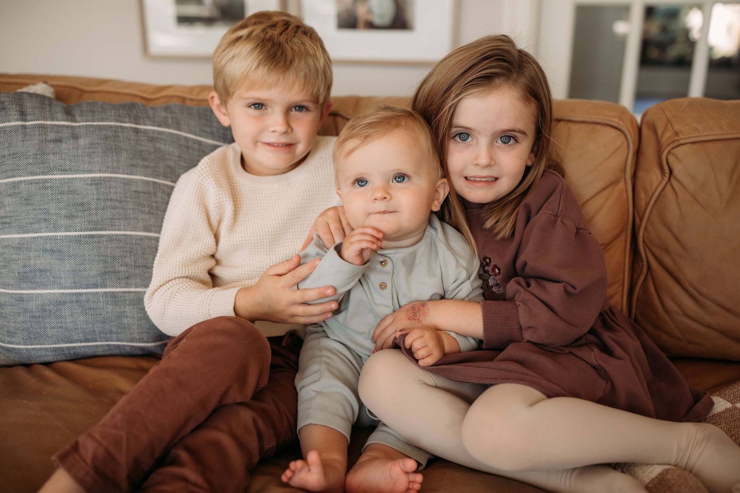 Three children sit together on a brown leather couch.