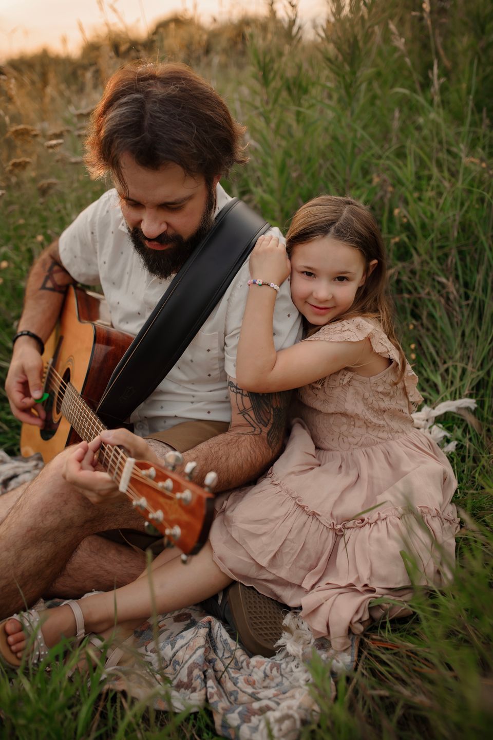 Sweet moment captured between guitarist and child sitting in tall grass.