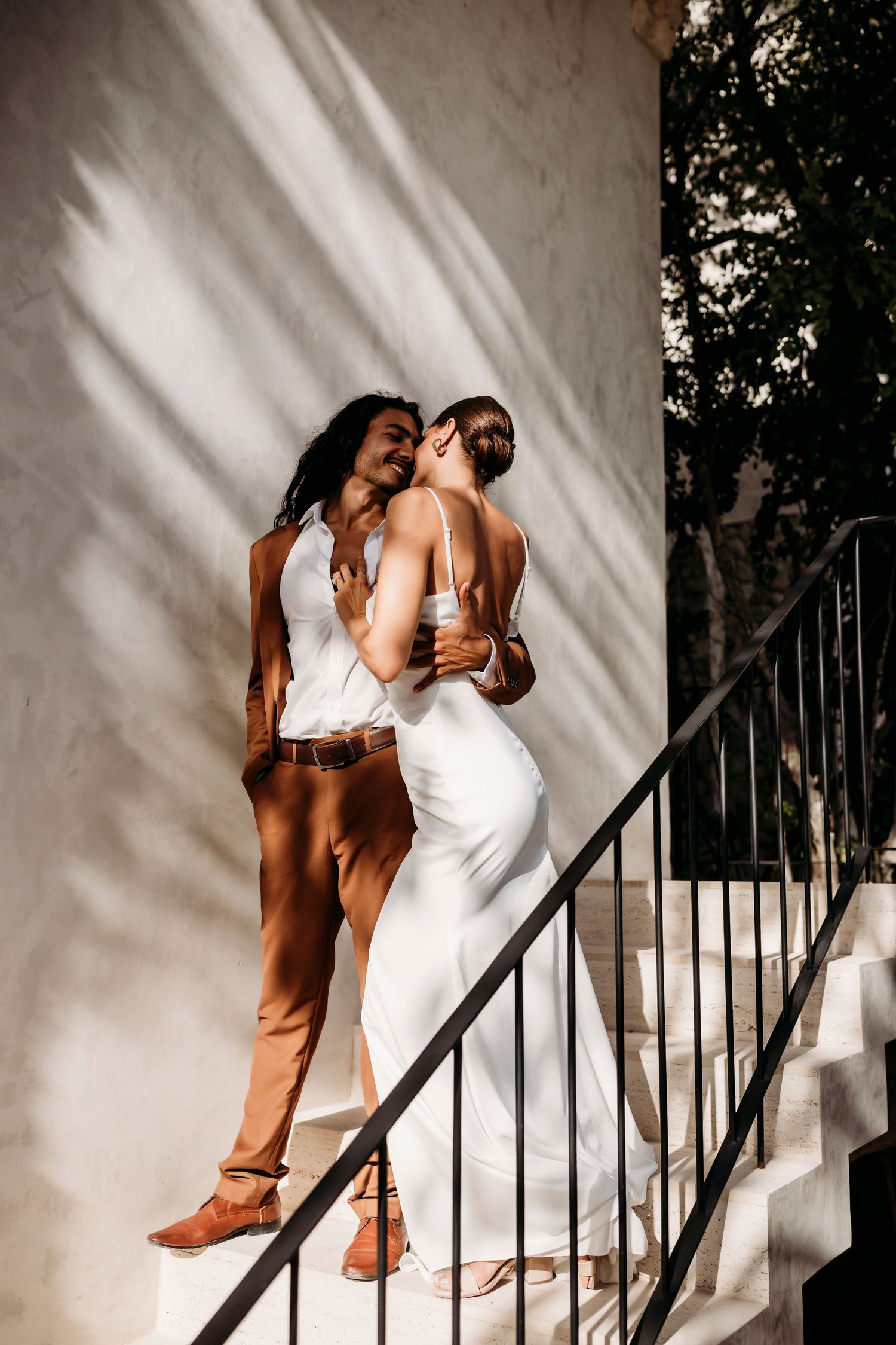 Couple embracing on white staircase with dramatic shadow play on wall.