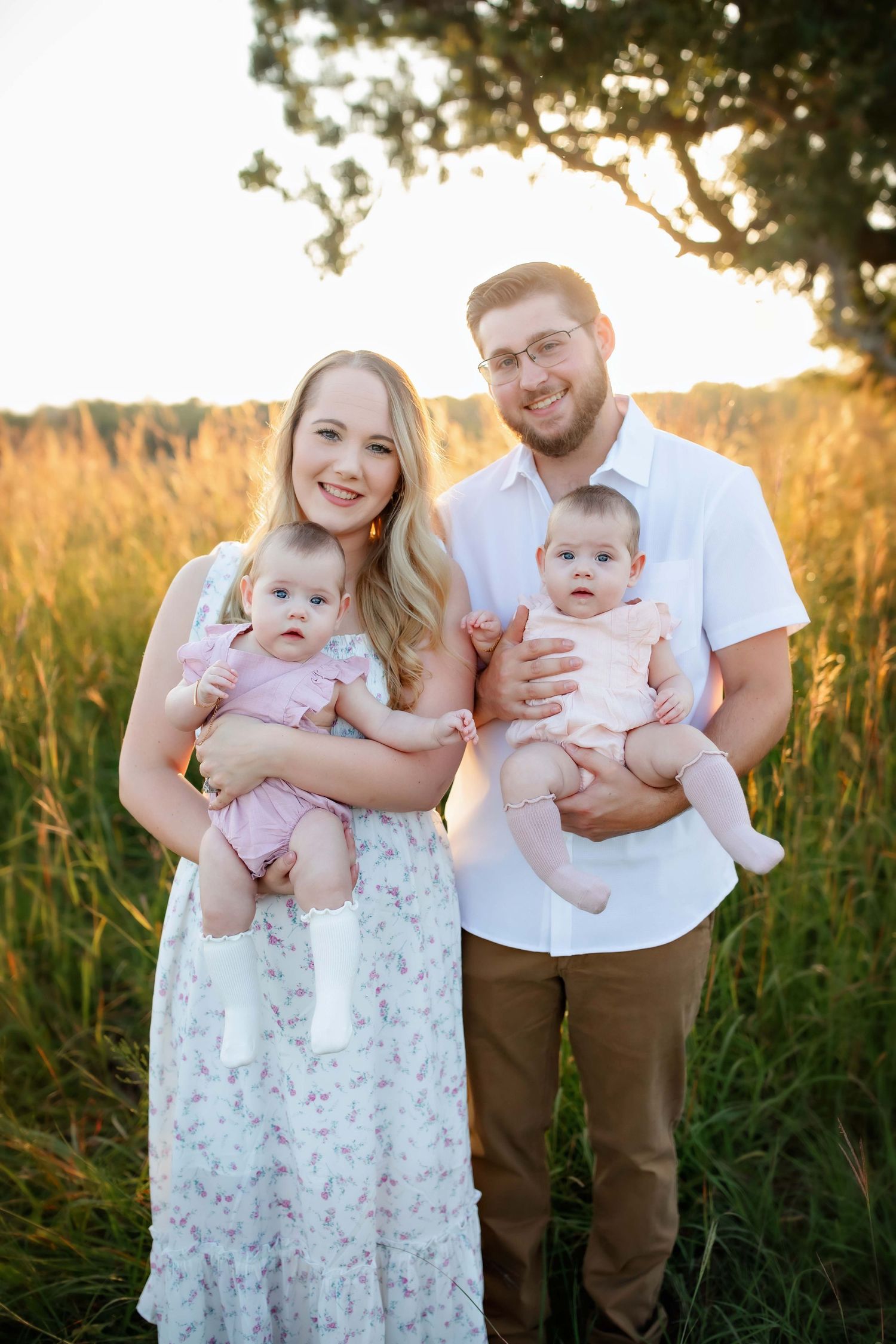 Family portrait in golden field at sunset with twin babies wearing matching outfits.