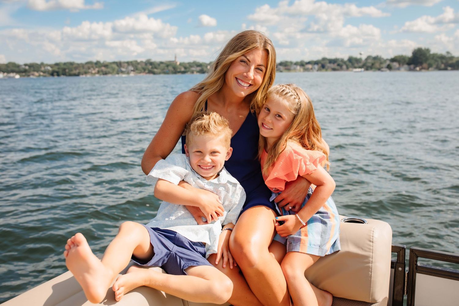 Family cuddles together on boat seating during lake day adventure.