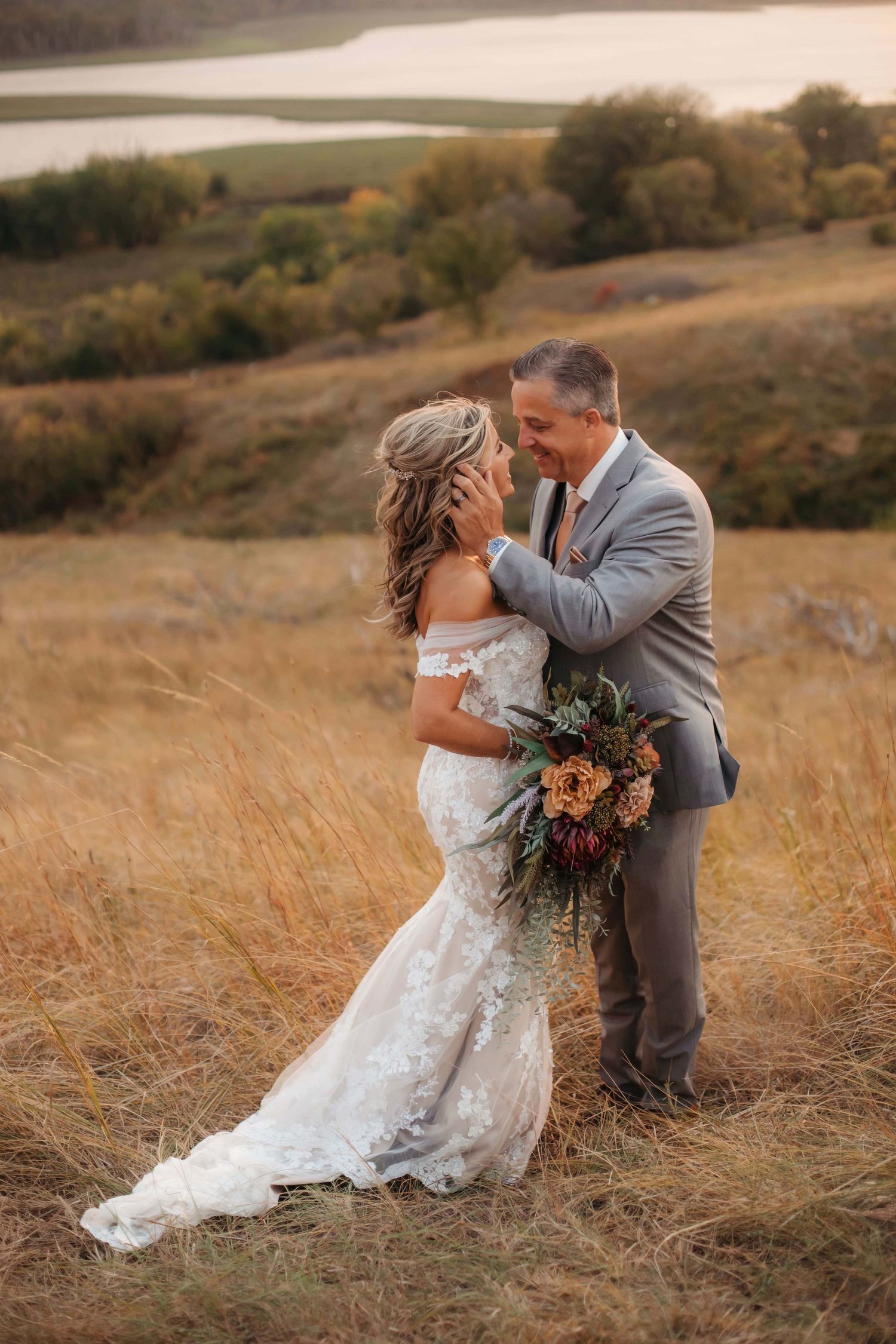 A tender moment between newlyweds in a golden field with lake views.