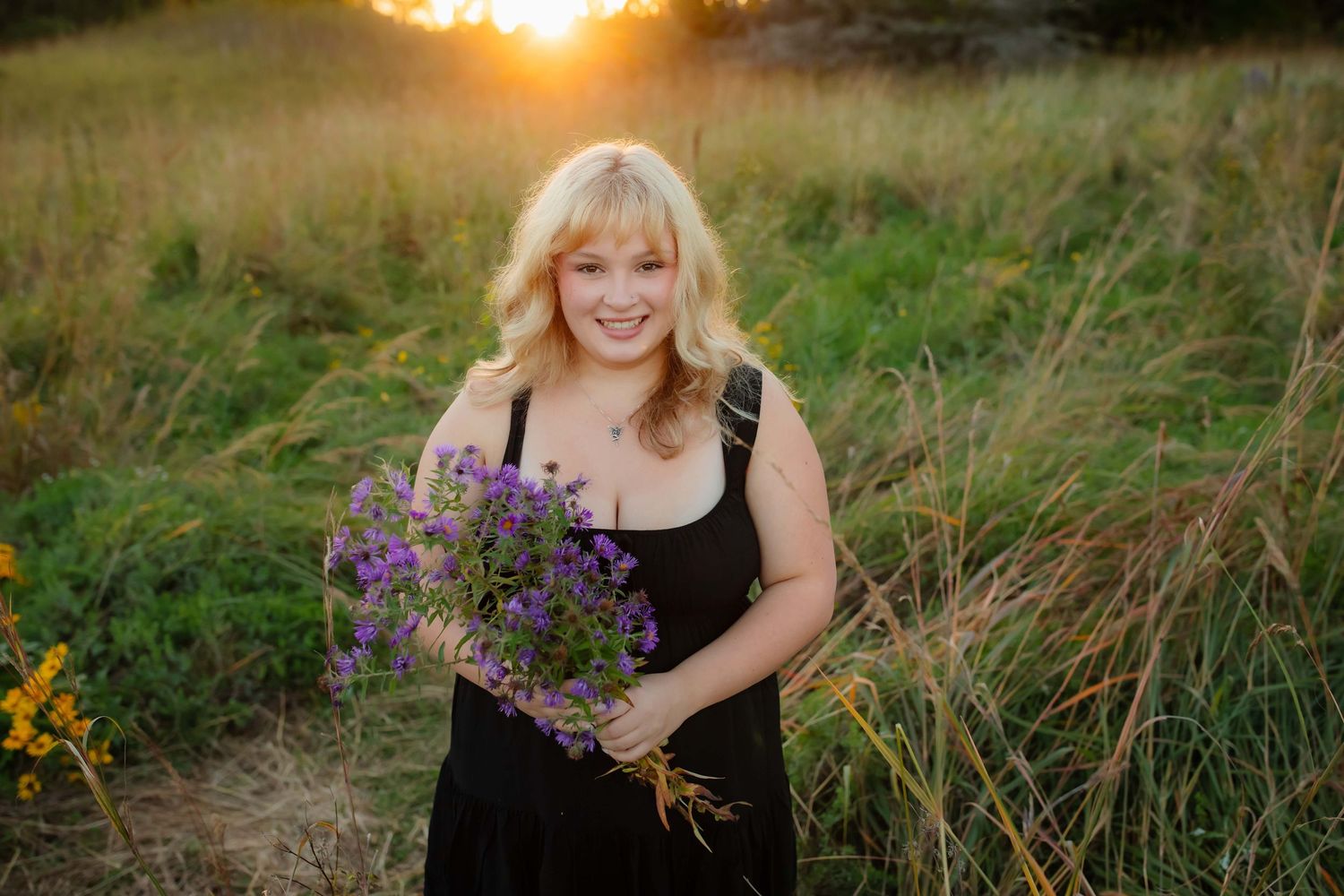 Person holding purple wildflower bouquet at sunset in field.