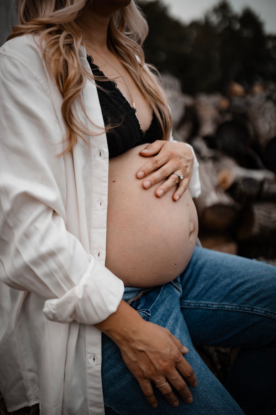 A maternity photo showing a pregnant belly with hands resting on it, wearing jeans and white button-down shirt.