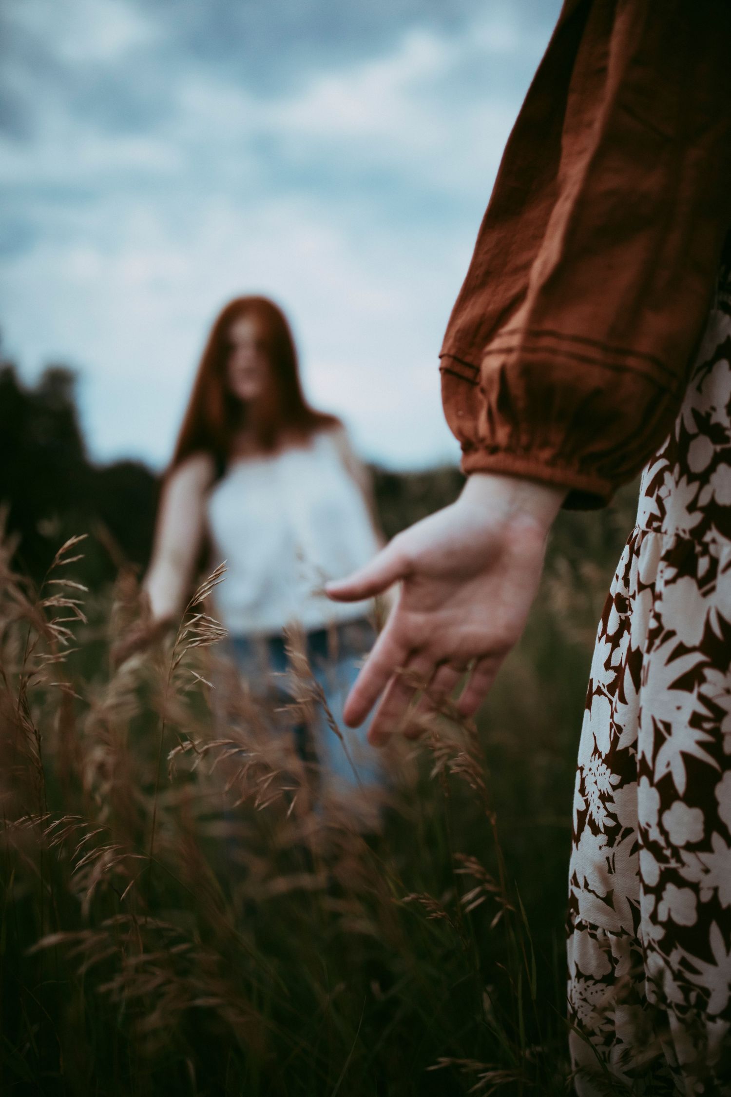 Artistic photo of hands and flowing dresses in a field of tall grass at sunset.