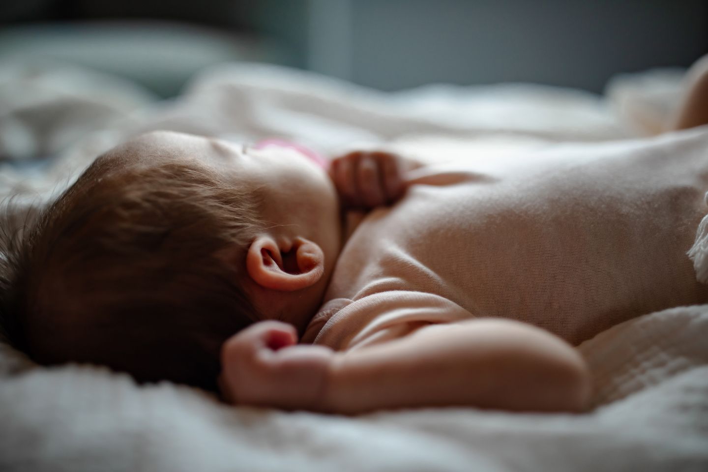 Side profile of sleeping infant on soft white bedding in natural light.