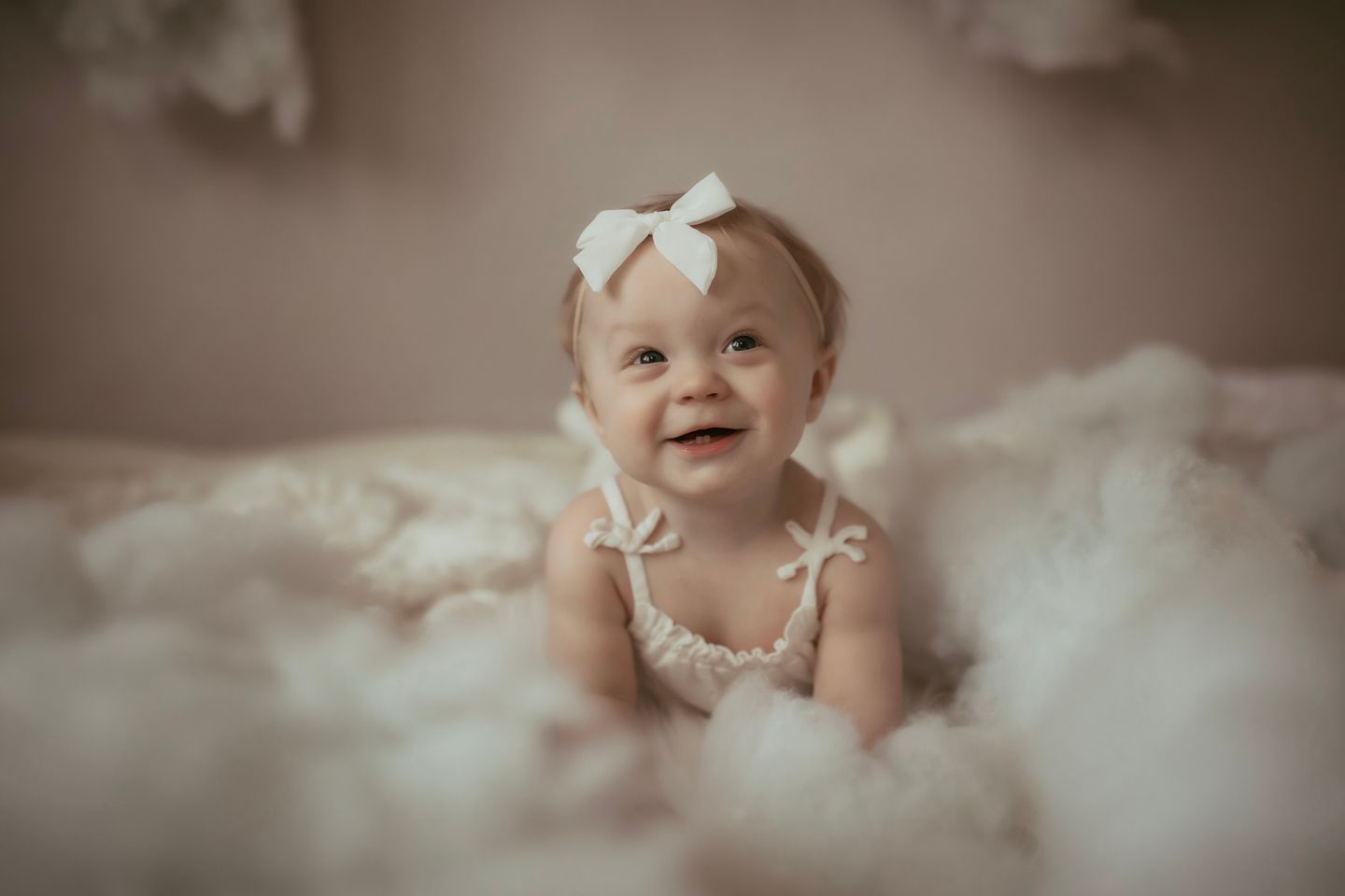 Baby in white dress smiling while surrounded by soft white textures.