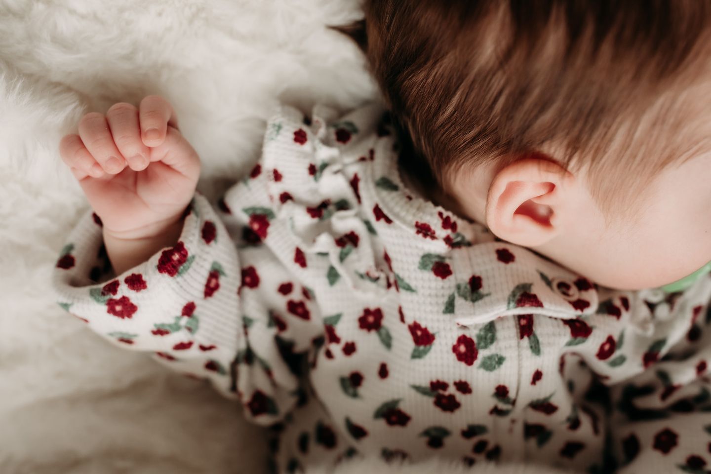 Close-up of tiny baby hand wearing floral print sleepwear against white textured background.