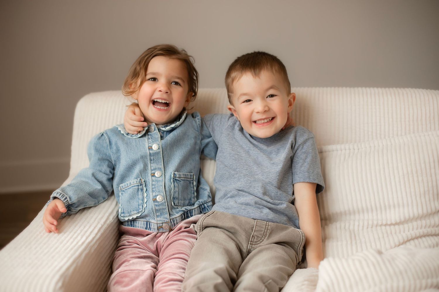 Children laughing and playing together while sitting on a white couch in a casual home setting.
