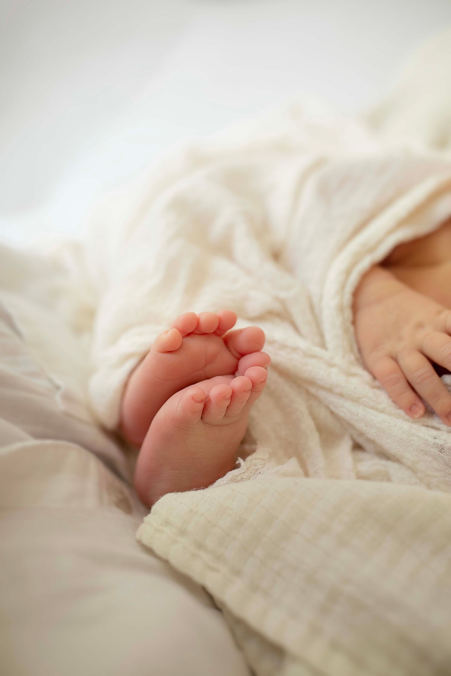 Close-up of tiny newborn baby feet wrapped in a soft white muslin blanket.