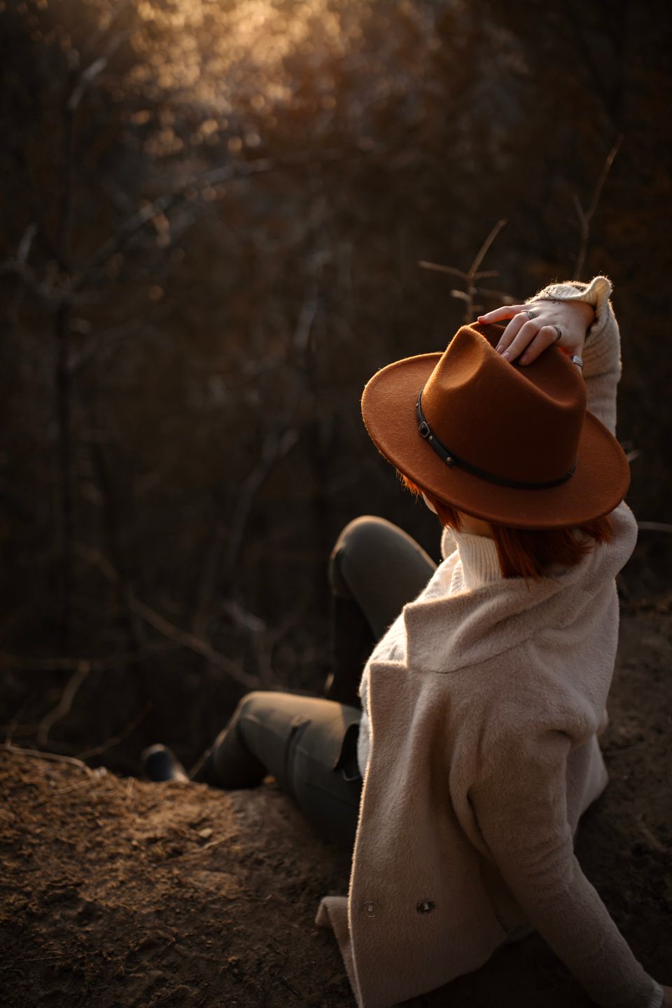 A person in a brown fedora and beige coat gazes into the distance at sunset.