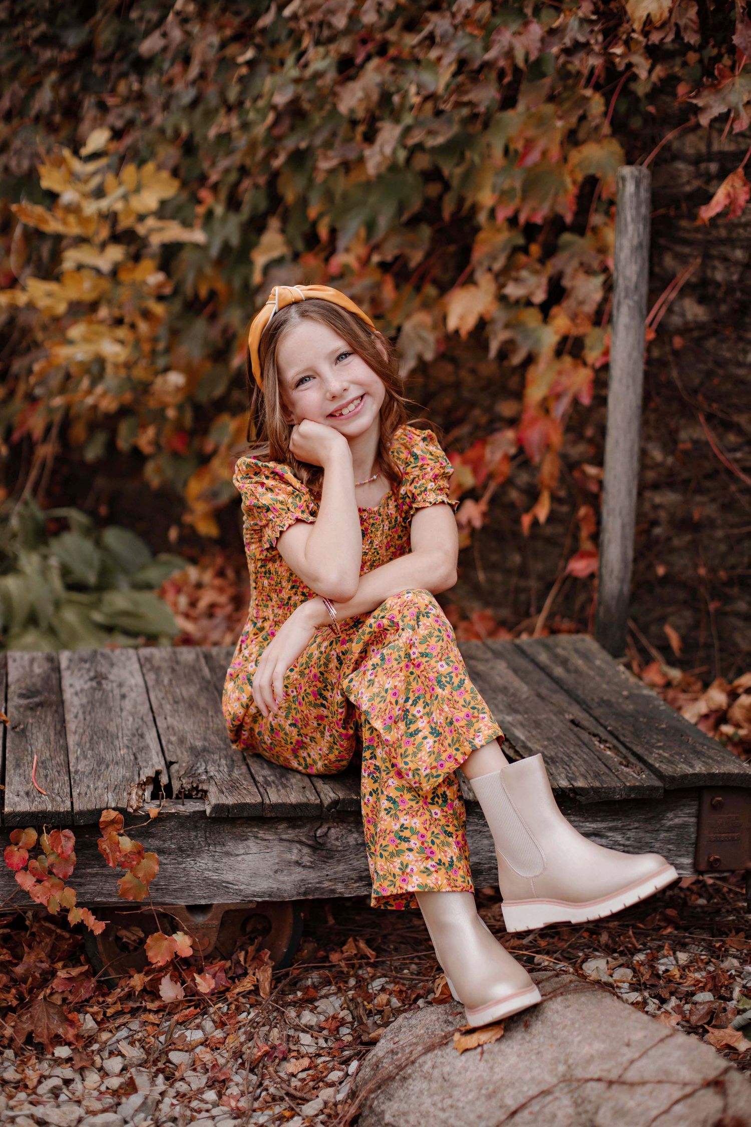 A cozy autumn portrait showcasing floral clothing and metallic boots against a backdrop of fall foliage.