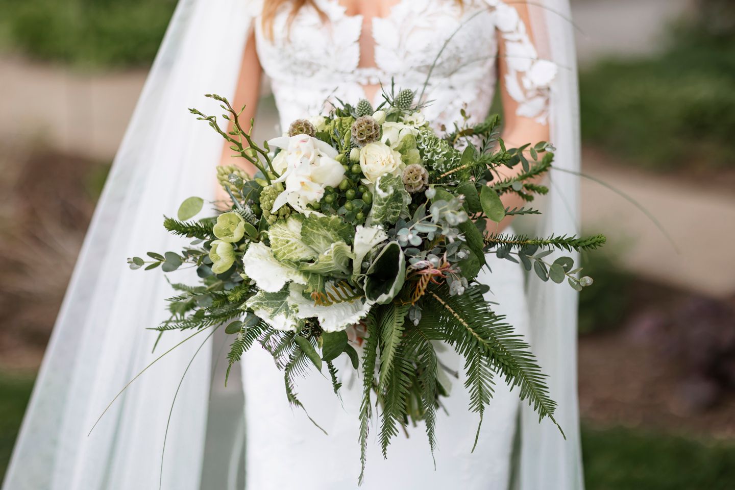 A lush white and green wedding bouquet with cascading foliage and textured greenery.