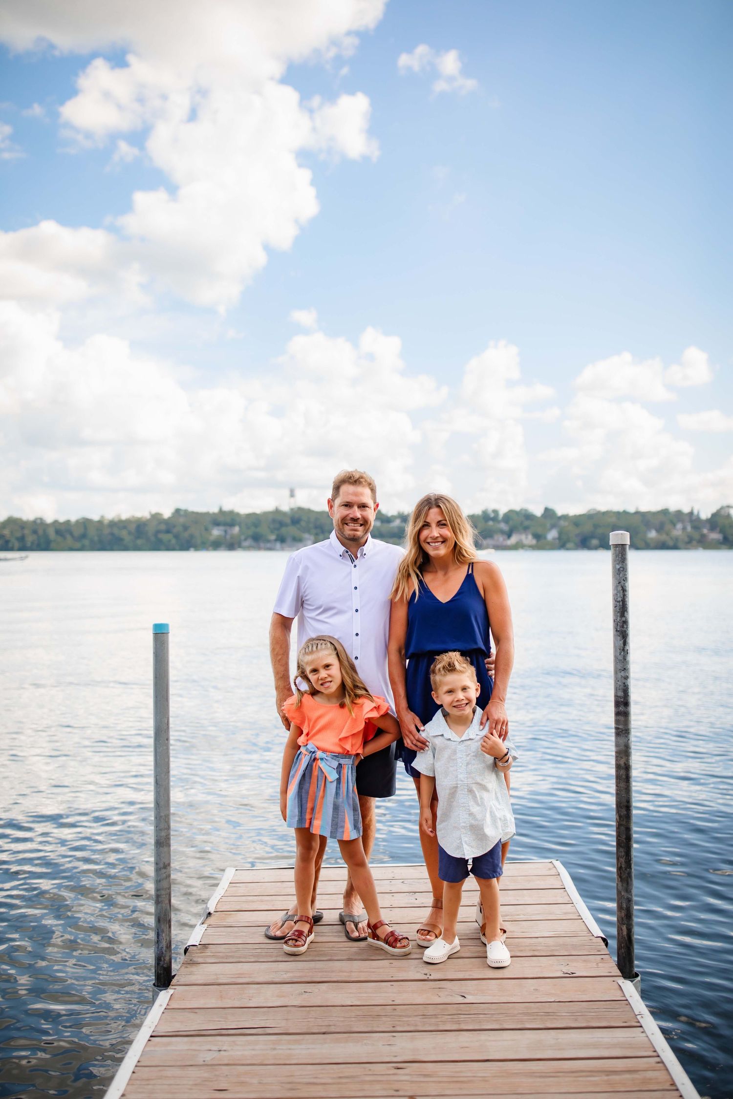 Family portrait on lakeside dock during bright summer day with blue skies.