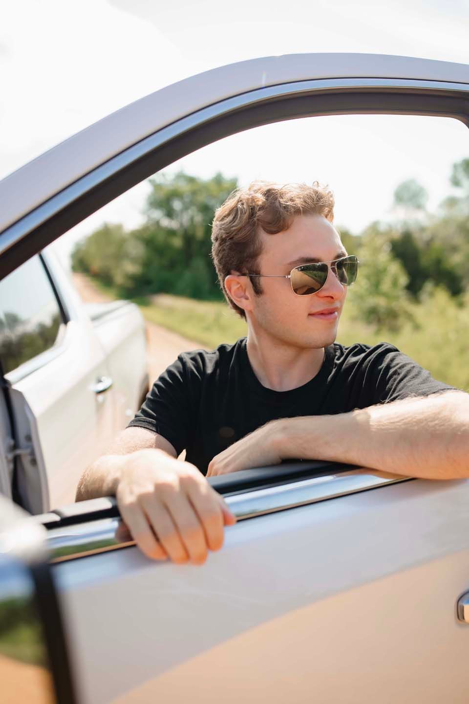 Person in sunglasses sitting in car with arm resting on window frame.