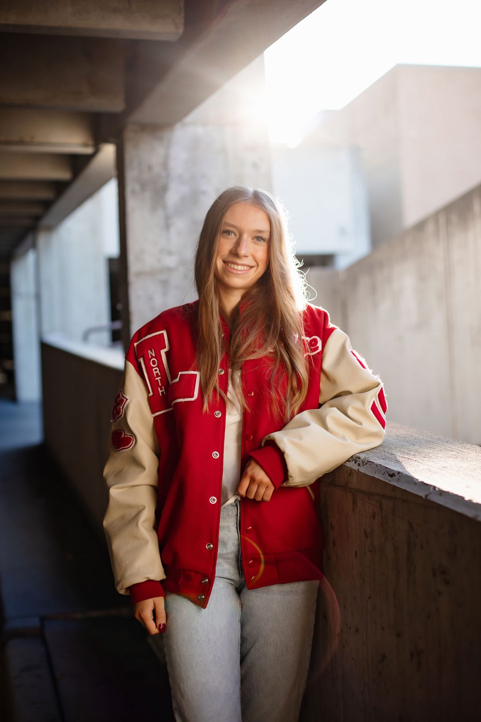 Stylish portrait wearing red and cream varsity jacket against concrete architecture.