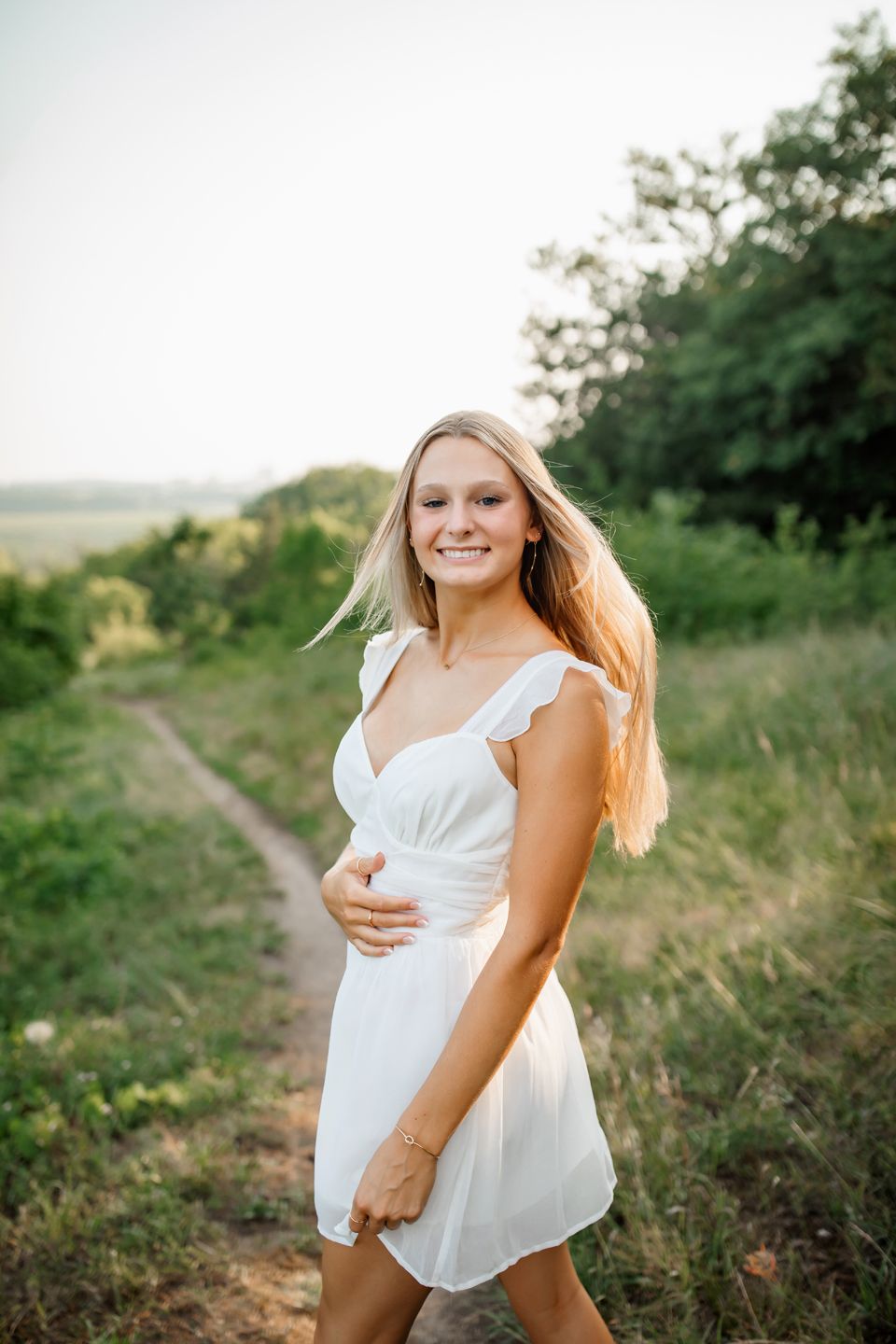 Someone in a white summer dress walking along a winding country path at sunset.