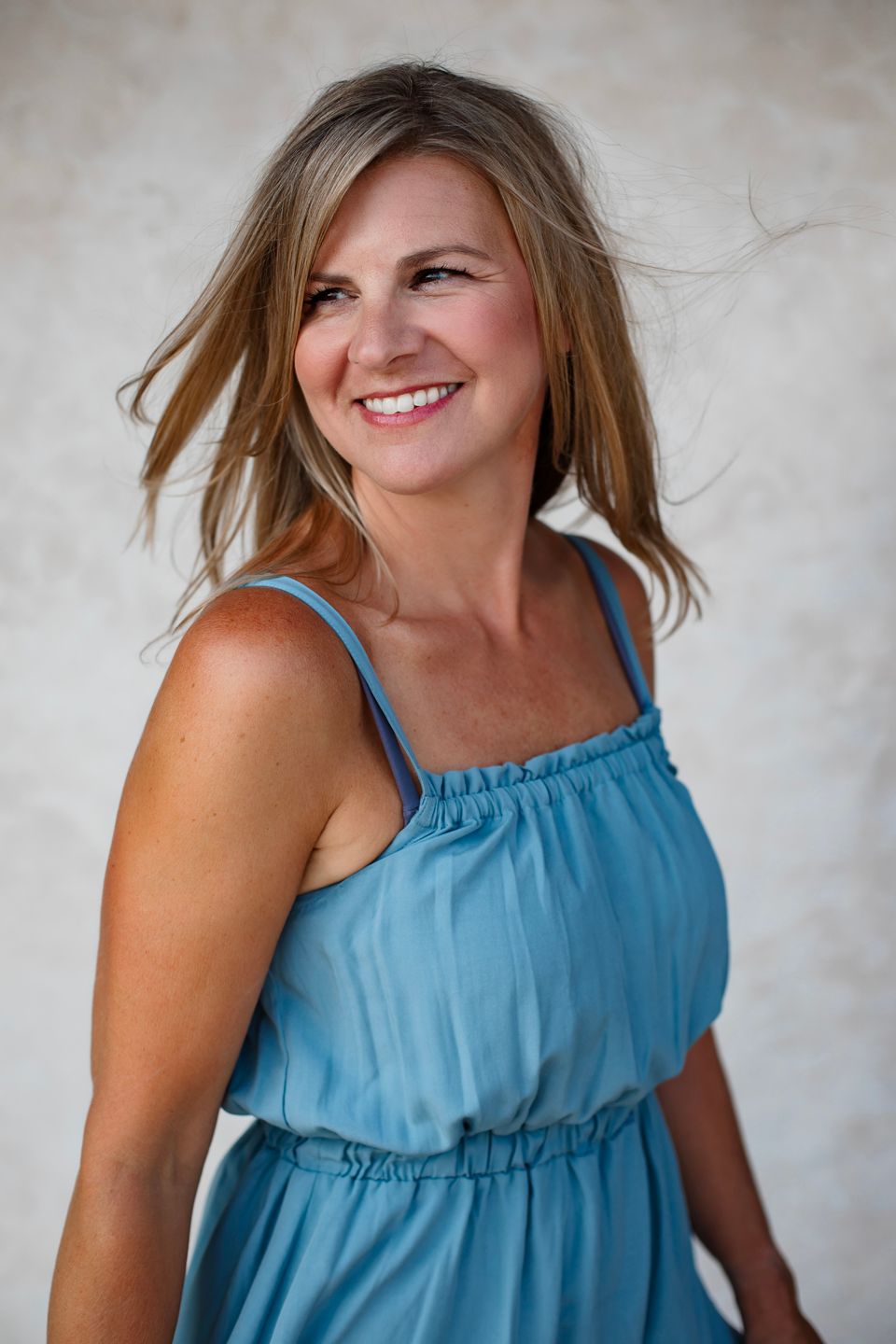 Lifestyle portrait with movement showing joy and laughter in casual blue summer dress.