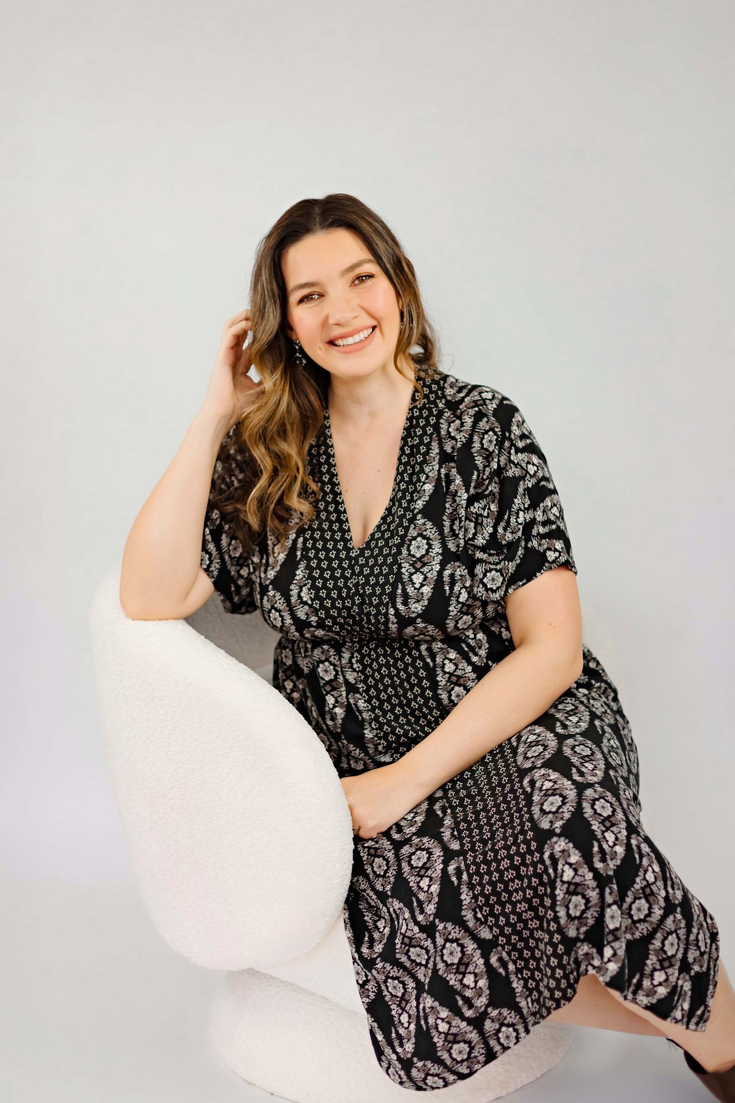 Casual pose in black and white floral patterned wrap dress on white chair.