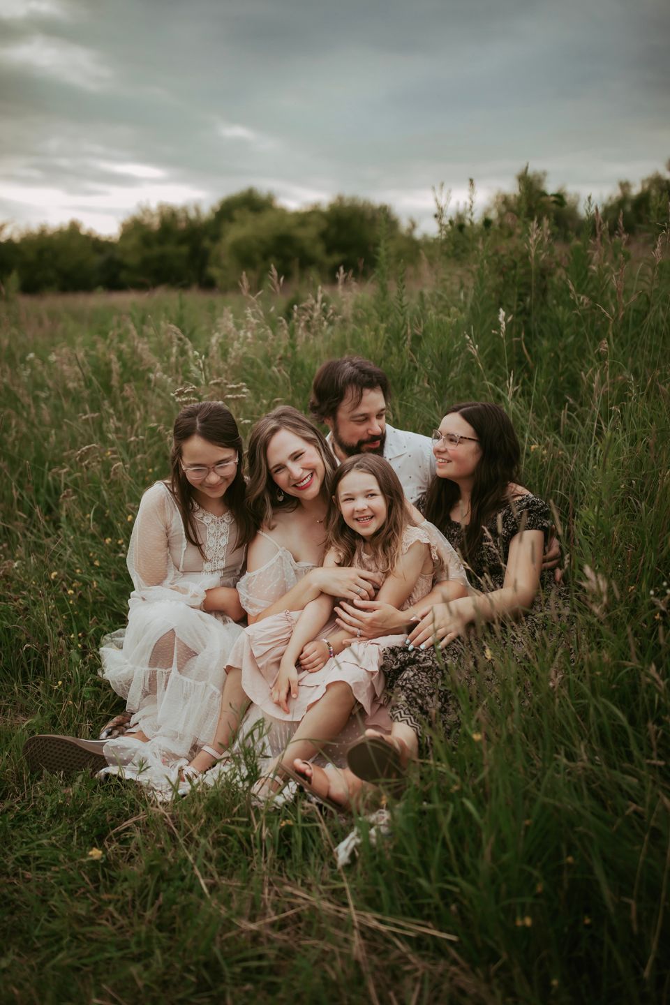 Family enjoying intimate moment together in tall grass field at dusk.