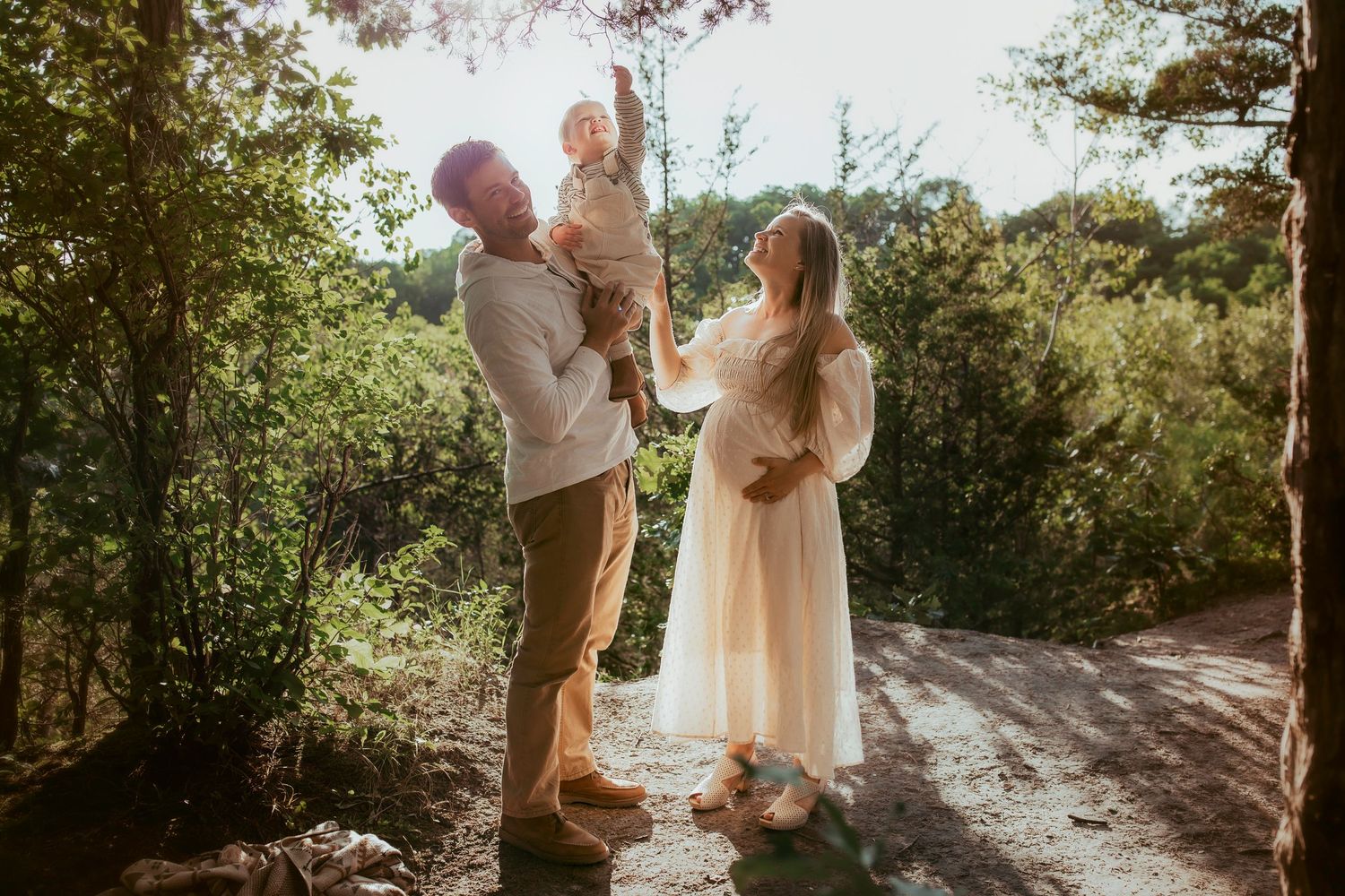 A sun-drenched family portrait in nature featuring soft white clothing and natural surroundings.