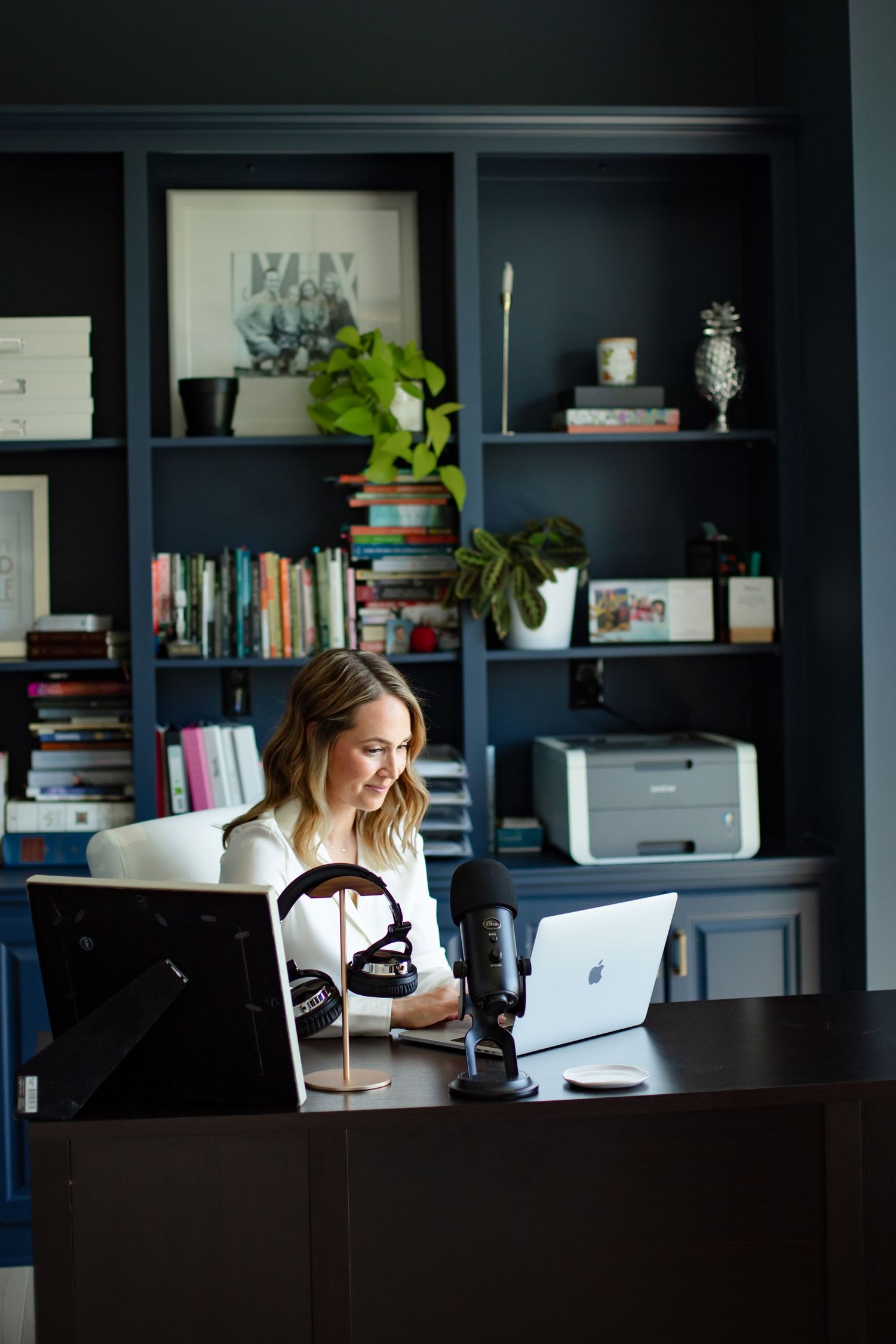 Home office workspace with dark built-in bookshelves and green plants.