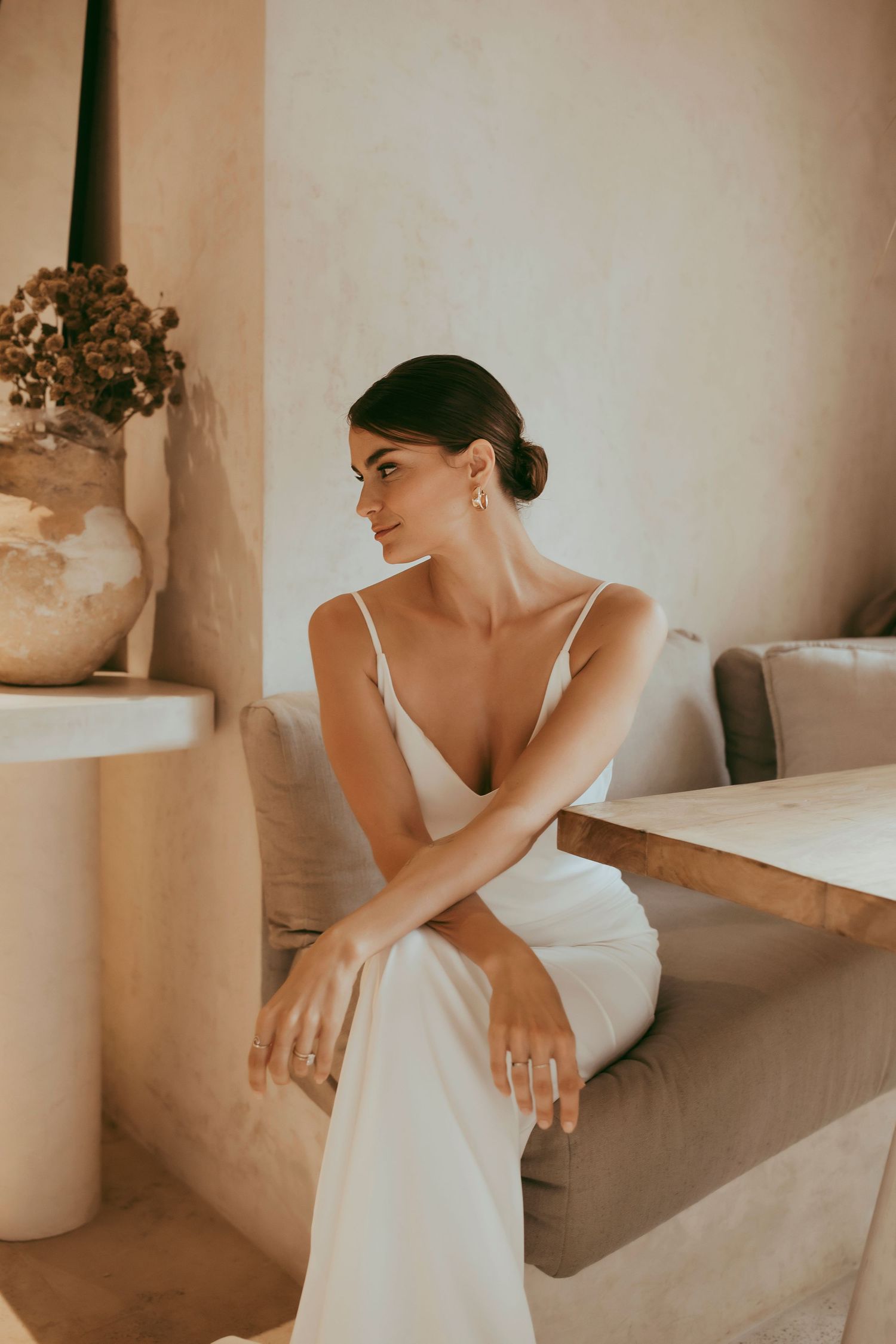 Woman in elegant white dress posed gracefully on beige sofa.