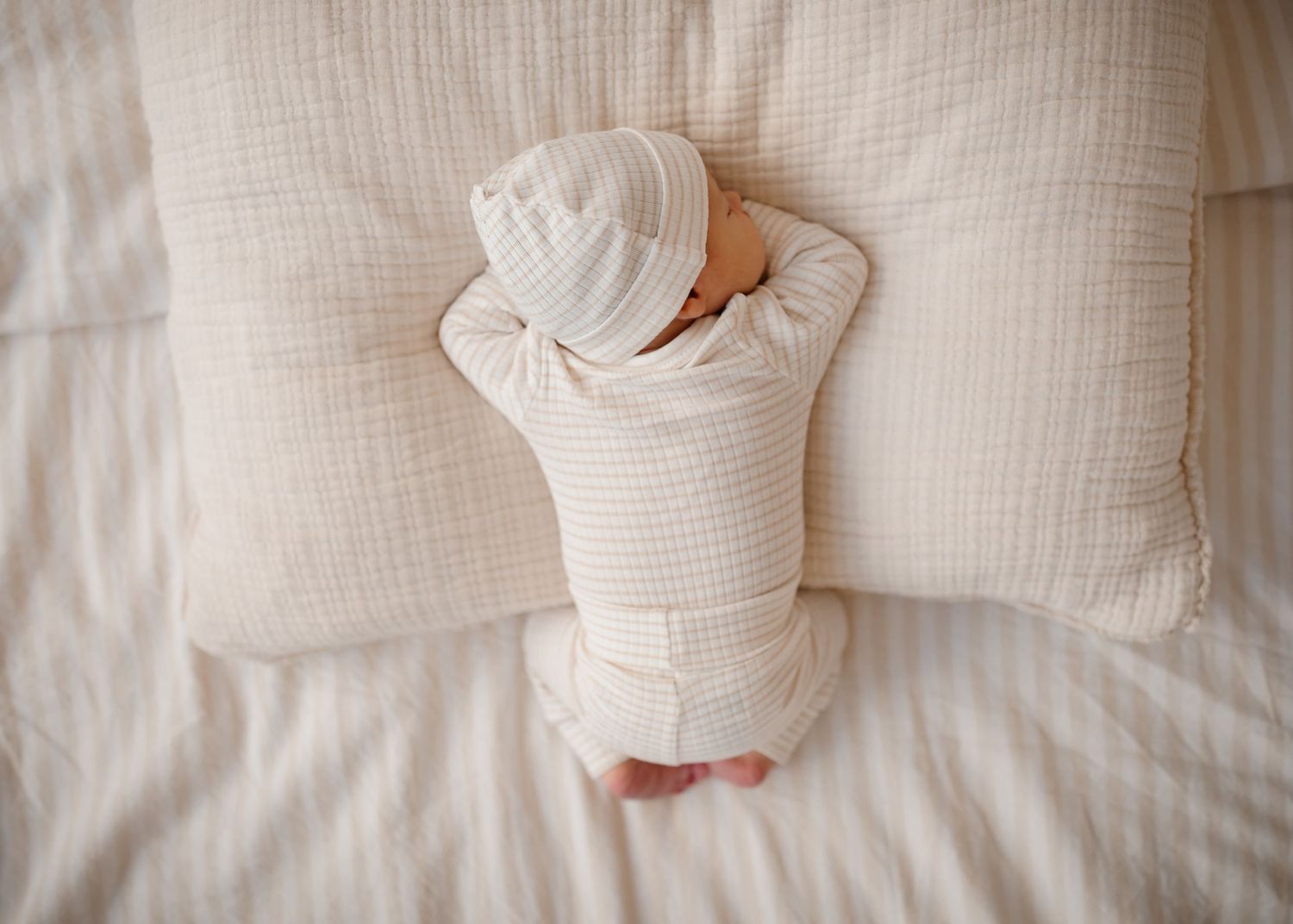 Newborn baby sleeping on white bedding wearing a white striped onesie and matching hat. Willow & Wren Photography newborn session.