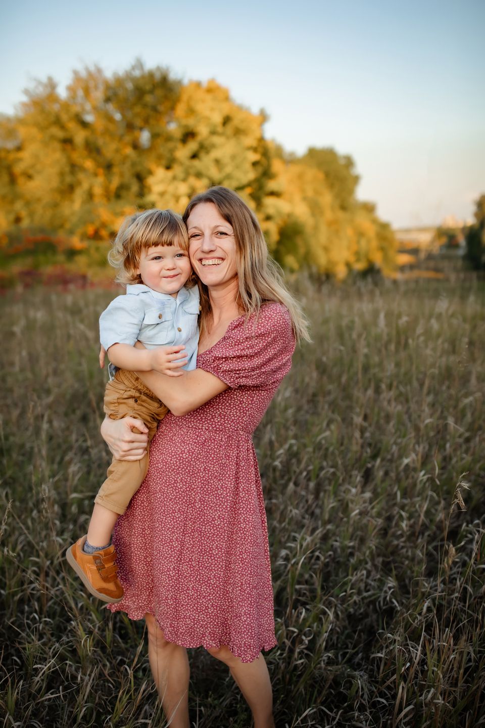A tender moment captured in a golden field at sunset with autumn trees creating a warm backdrop.