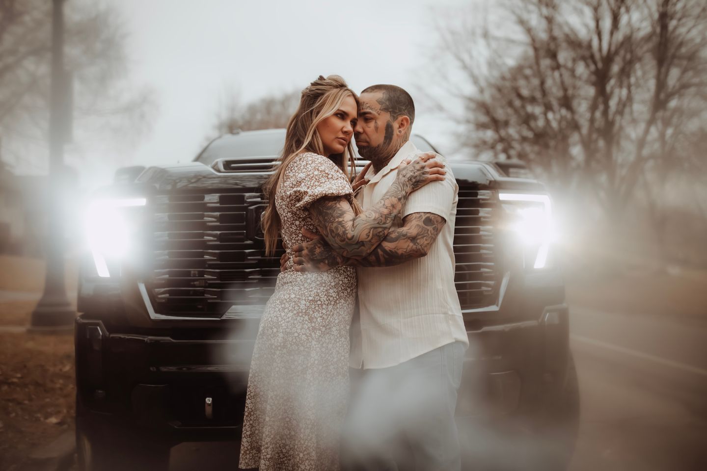 A romantic couple embraces near a vintage truck in a dreamy sepia-toned outdoor setting.