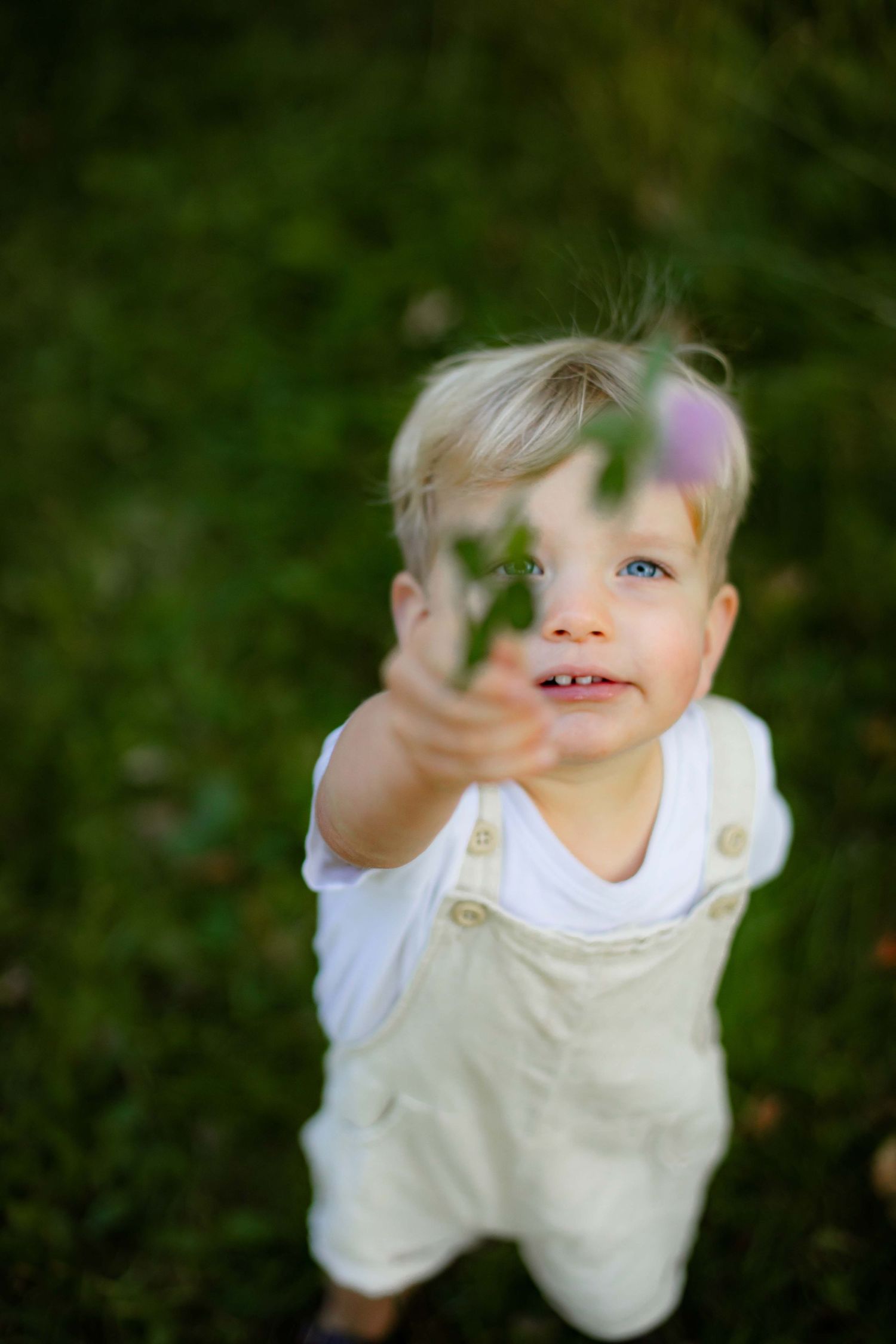 Looking up view of a child in white clothing against a green forest background.