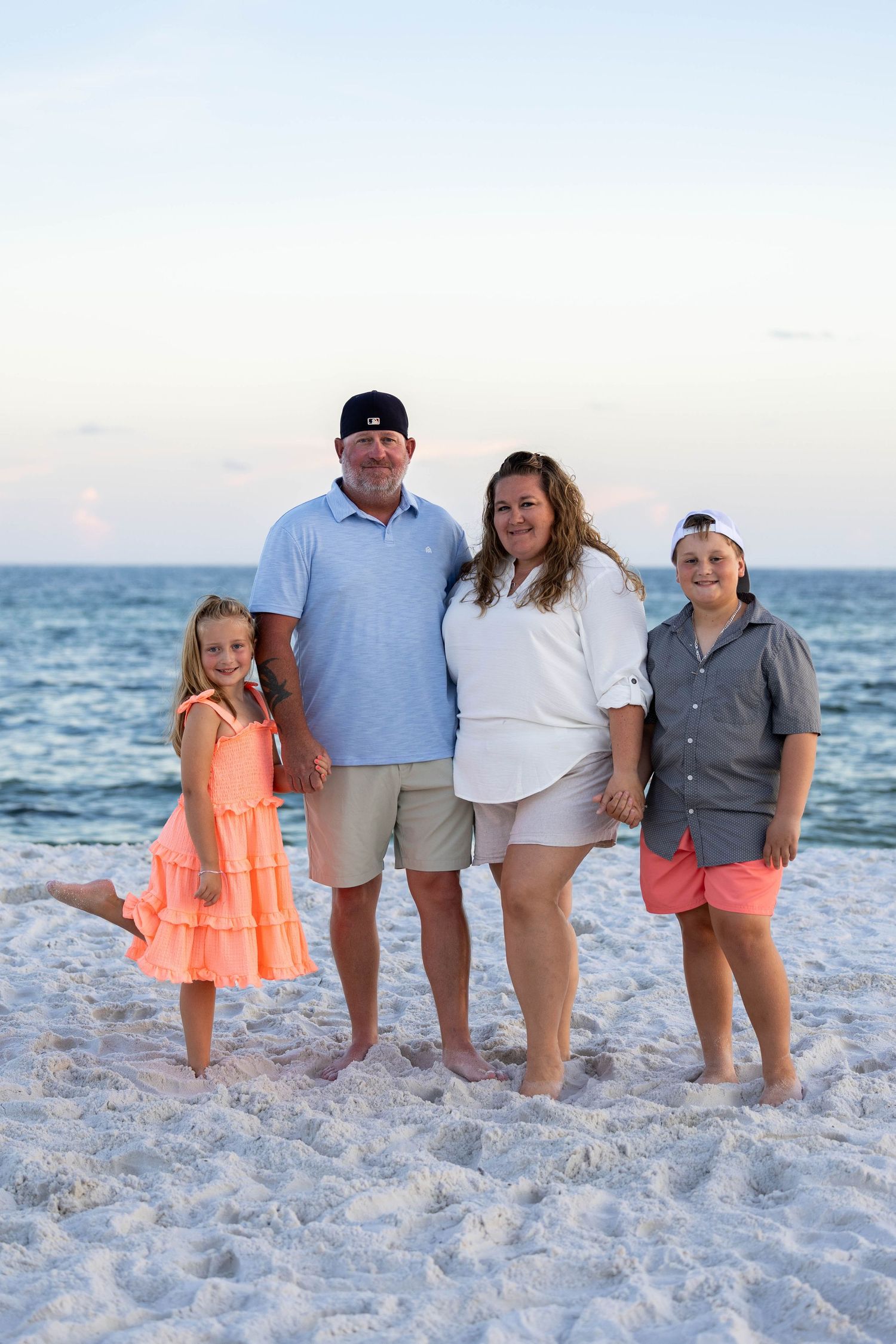 Family group portrait on white sandy beach at sunset.