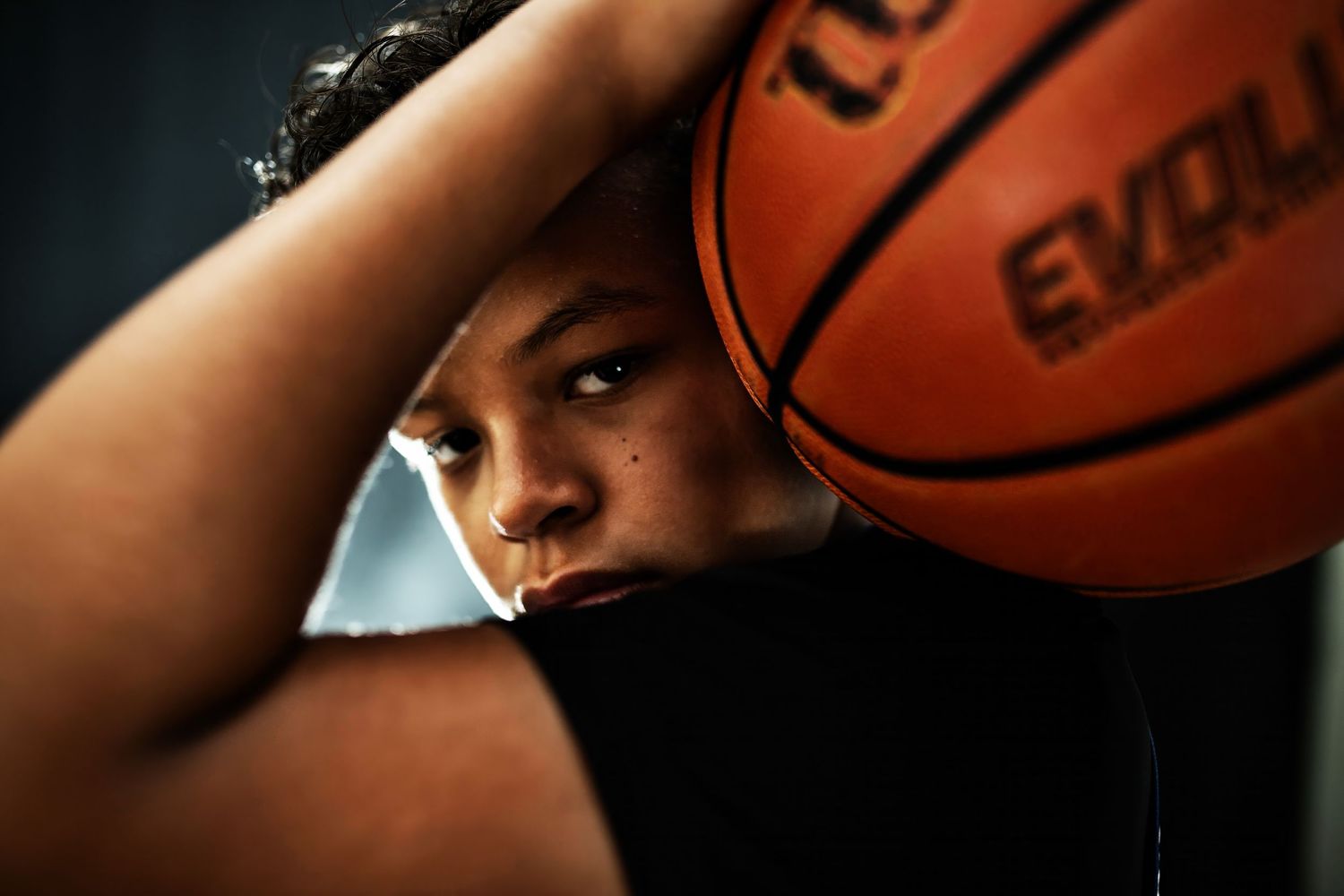 A dramatic close-up portrait of a basketball player with a ball against a dark background.