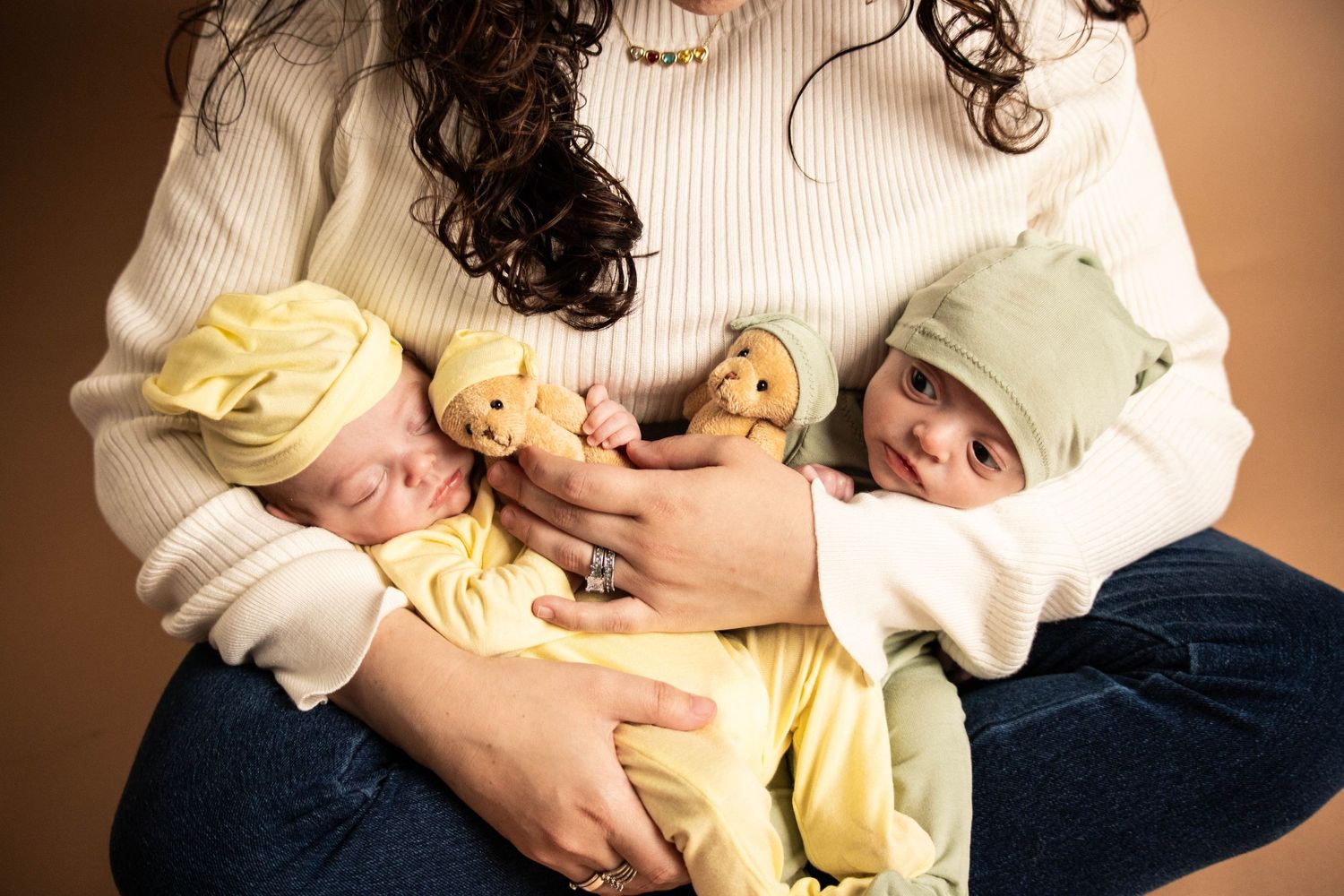 Three sleeping babies in yellow outfits held together in loving embrace.