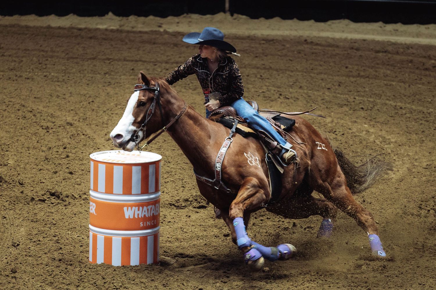 Horse and rider making tight turn around orange and white barrel during competition.