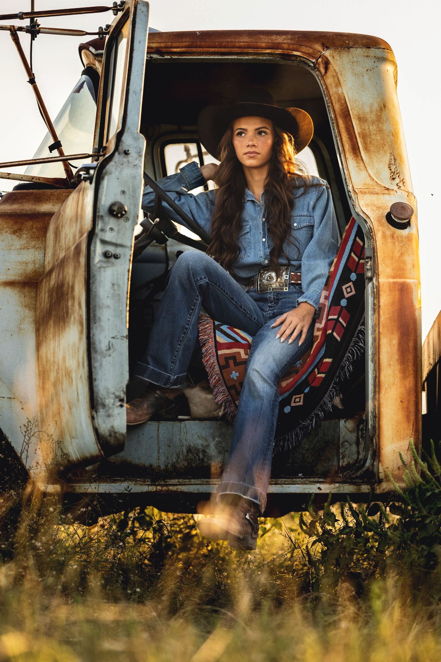 Rustic portrait in vintage truck wearing denim and western hat.