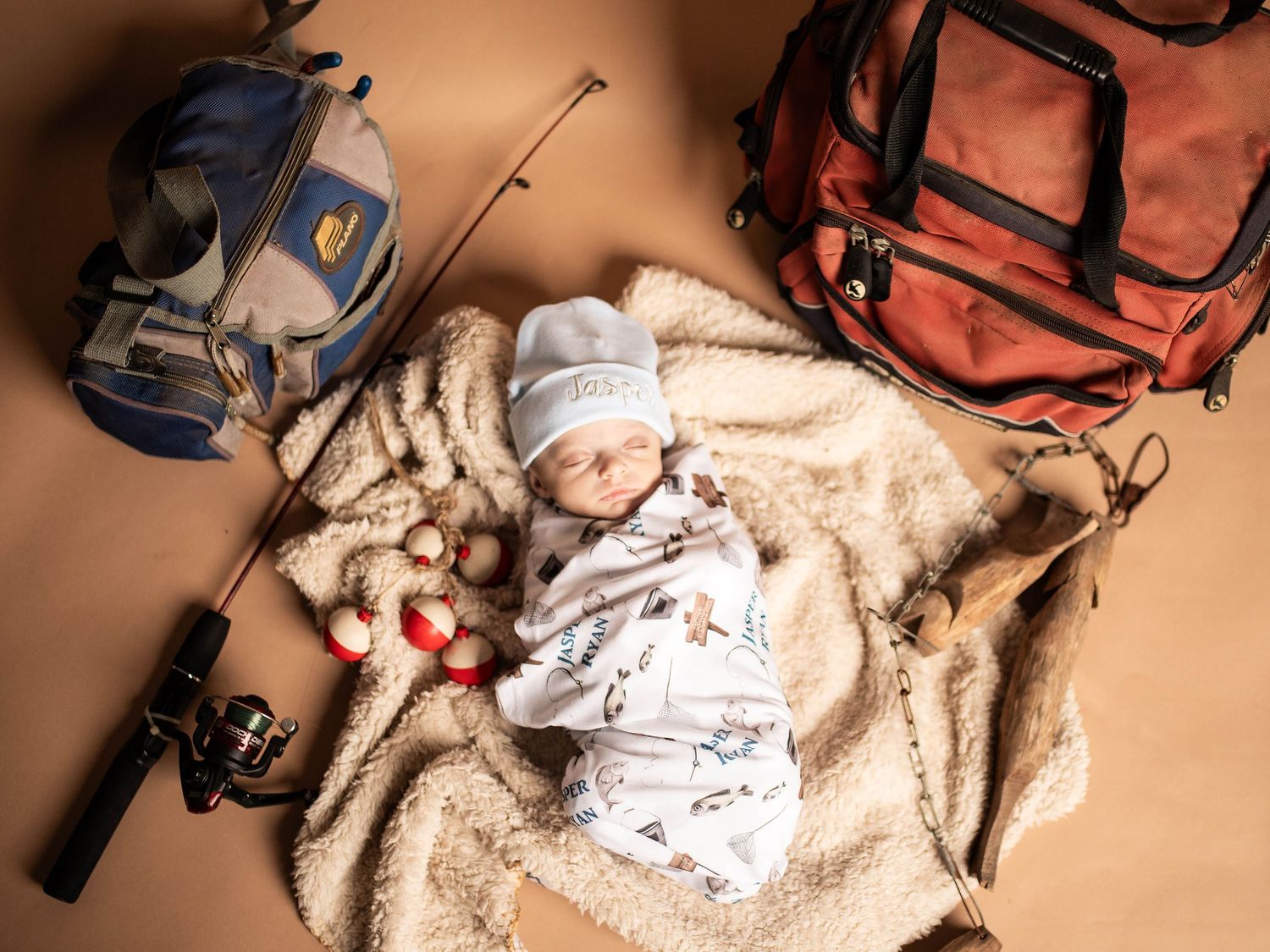 Sleeping baby on blanket surrounded by fishing gear and outdoor equipment.