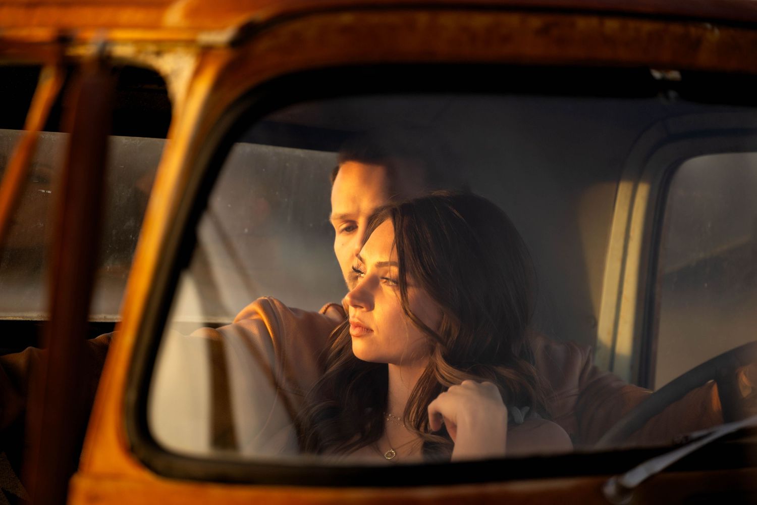 A couple shares an intimate moment inside a vintage orange truck at sunset.