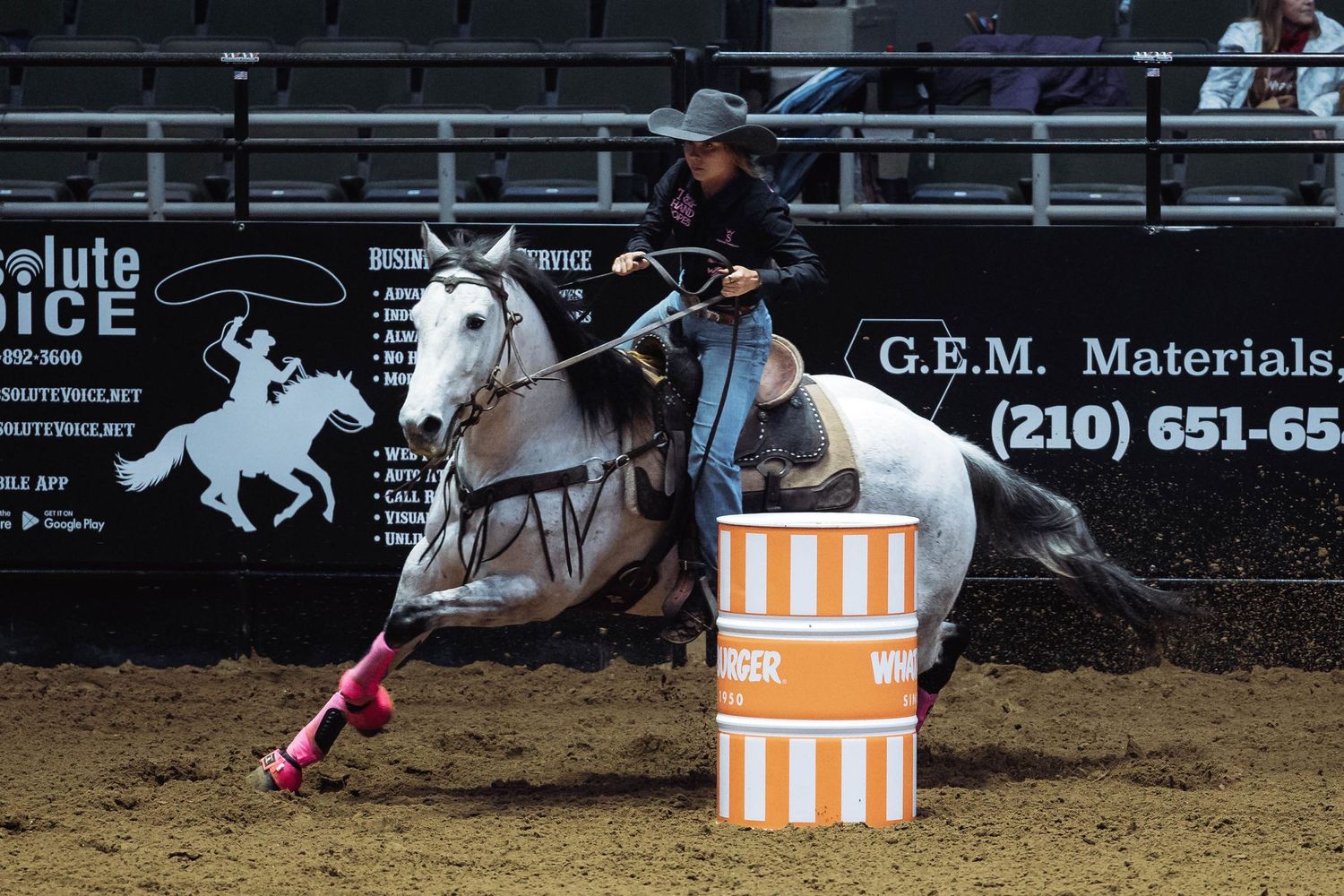 White horse and rider navigating barrel racing course at indoor rodeo arena.