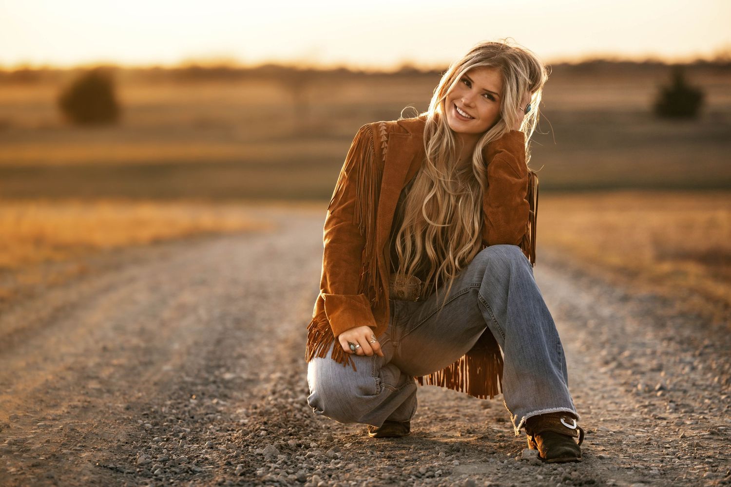 Warm sunset portrait in brown fringe jacket on dirt road.