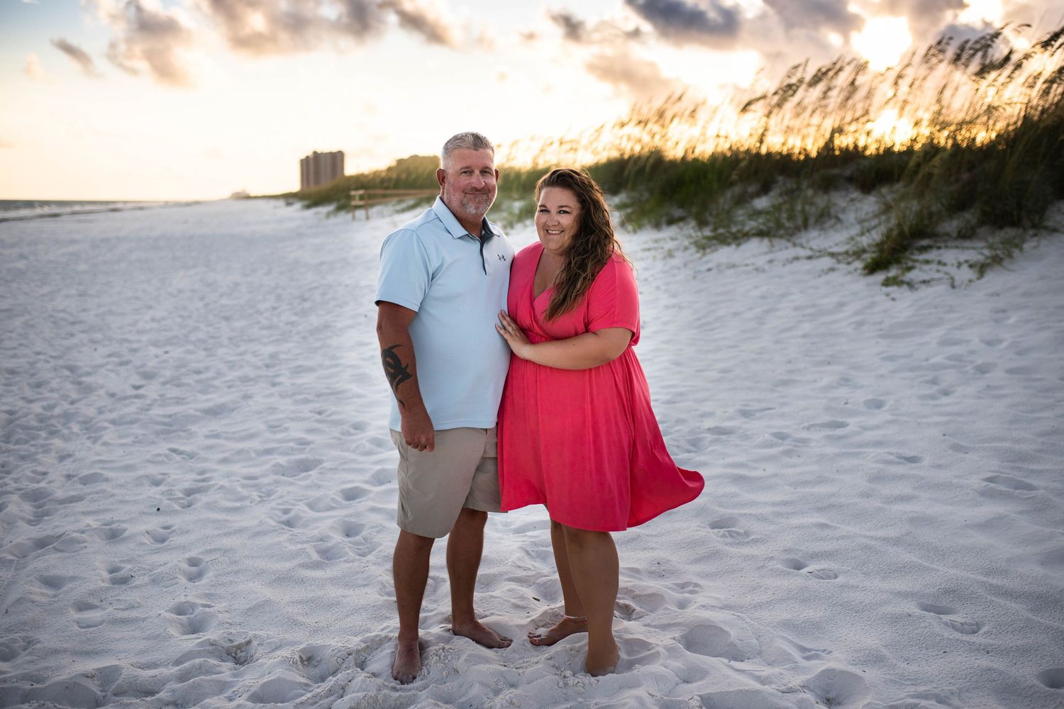 A scenic beach portrait at sunset with sand dunes and coastal buildings in the background.