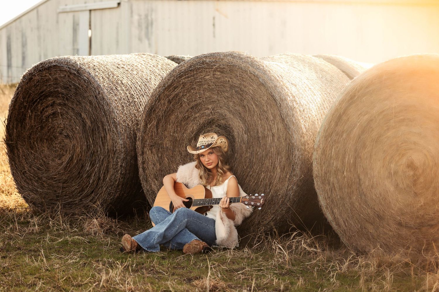 A country scene with large round hay bales at sunset creates a rustic farm setting.
