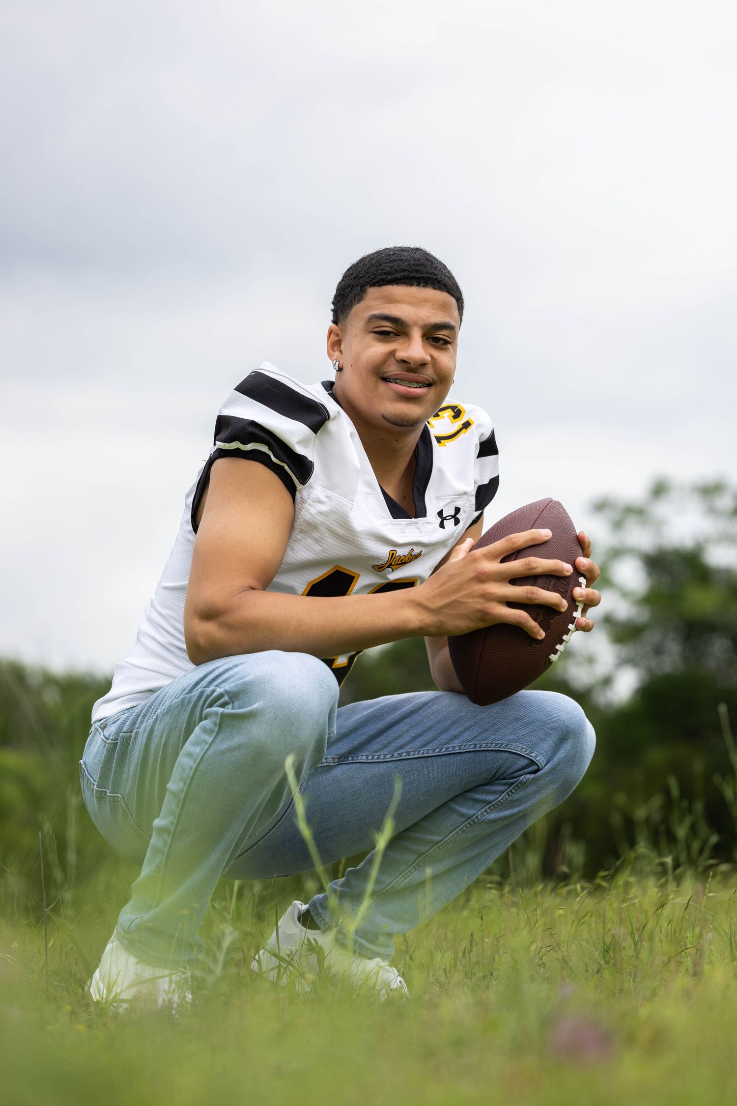Person in athletic wear crouches in a grassy field holding a football.