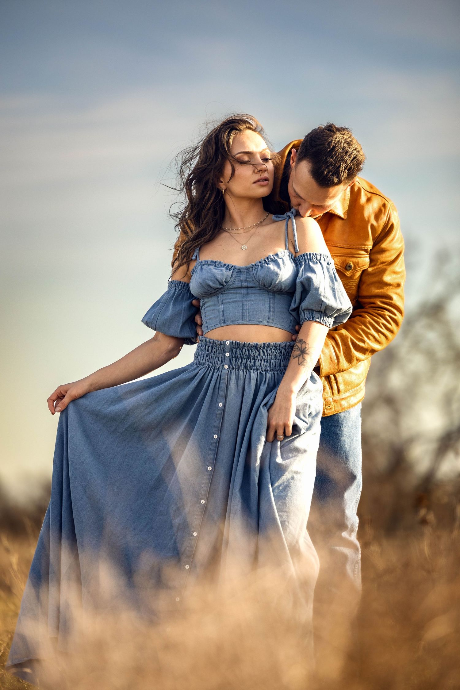 Romantic couple embracing in field during sunset with dreamy lighting.